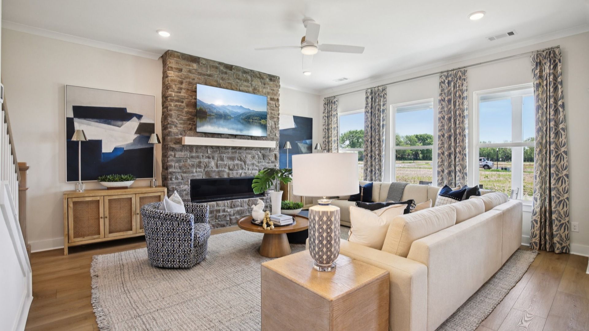 Large living room setup centered around stone fireplace with abundant natural light