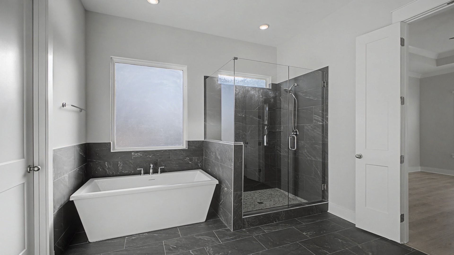 Large en-suite primary bath with tiled floor, double vanity, glass shower, and freestanding tub