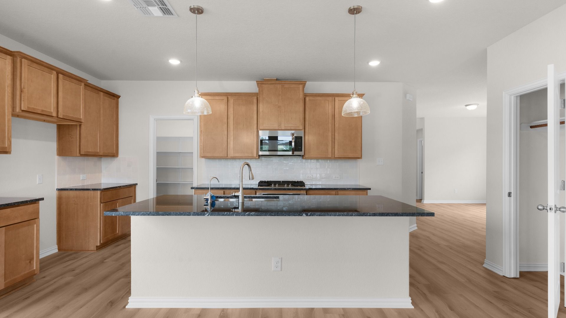 Black countertops, Tan 42 inch Cabinets, Gas Cooking, Pendant Lighting, Stainless Steel Appliances, Pantry, Coat Closet