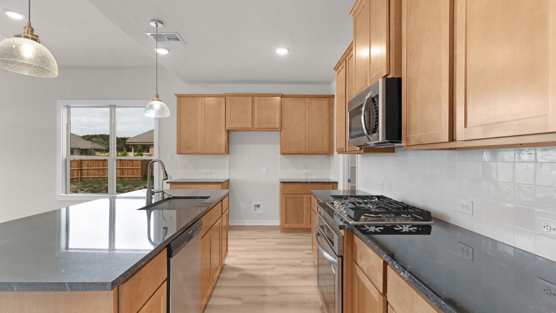 Black countertops, Tan 42 inch Cabinets, Gas Cooking, Pendant Lighting, Stainless Steel Appliances