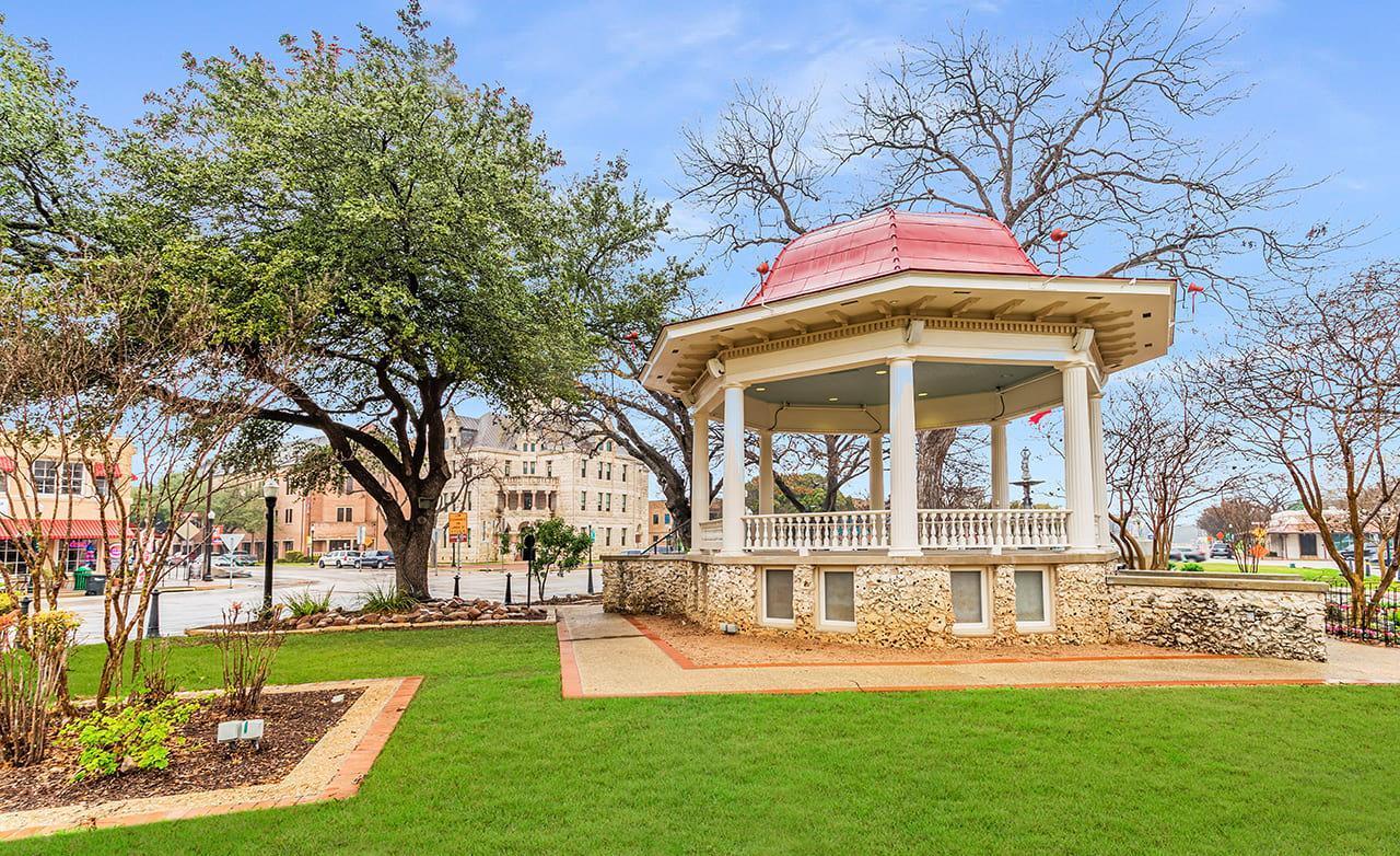 Elegant gazebo with intricate stone foundation and pillars, nestled in serene park, embodying timeless allure.