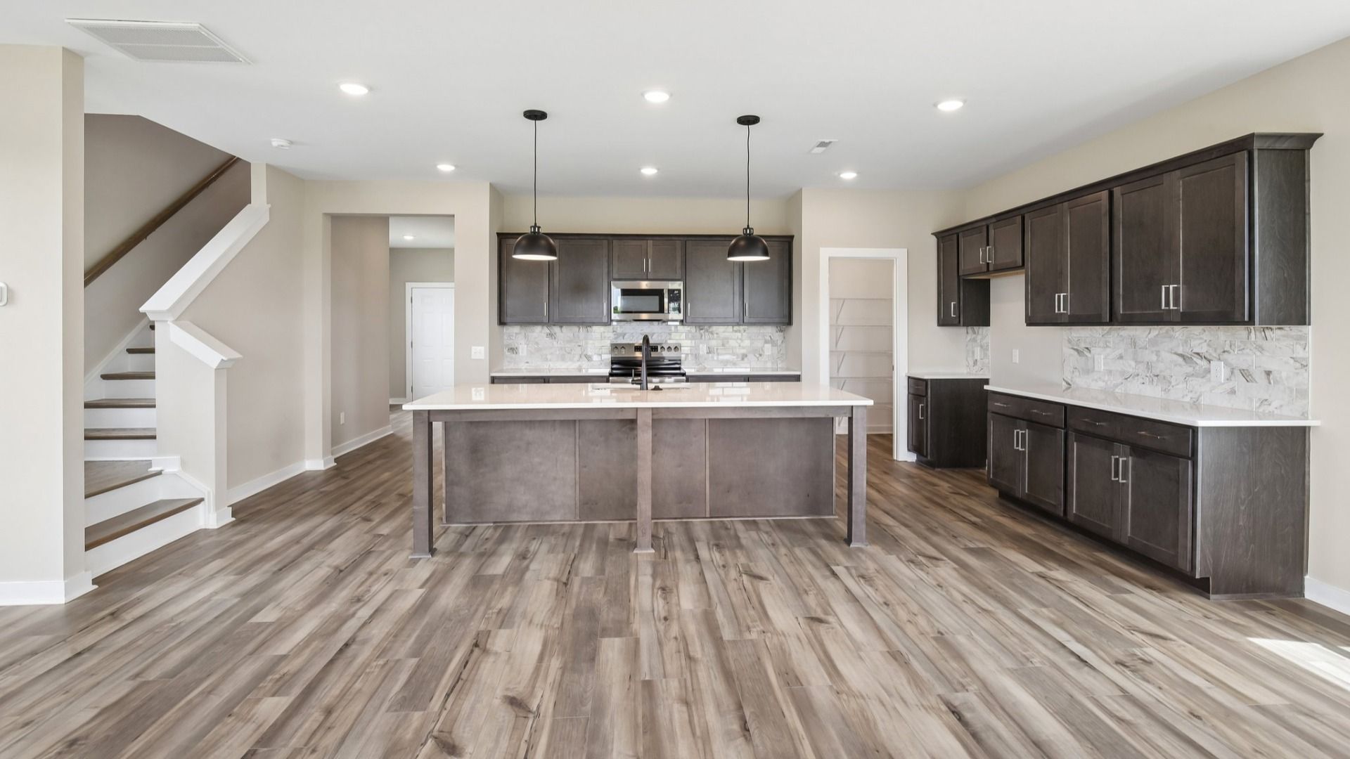 Kitchen with dark cabinetry, quartz countertops, and tile backsplash nearby staircase