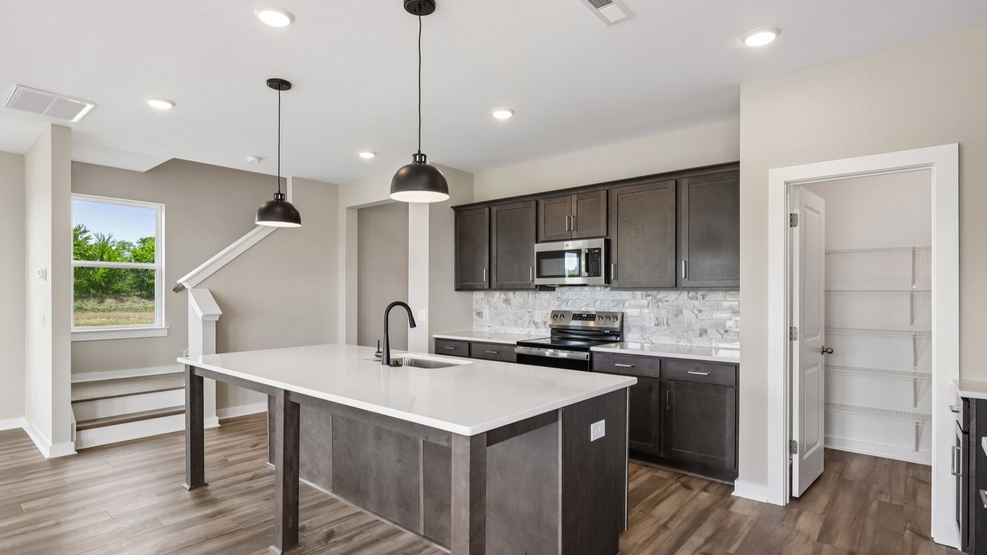 Kitchen with dark cabinetry, quartz countertops, and tile backsplash and pantry