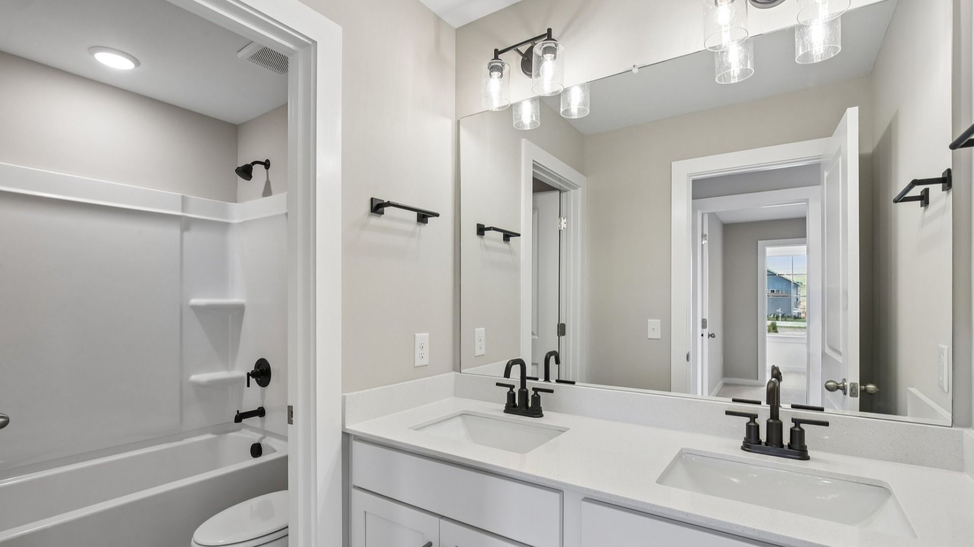 Secondary bathroom with dual vanity and door to shower and toilet