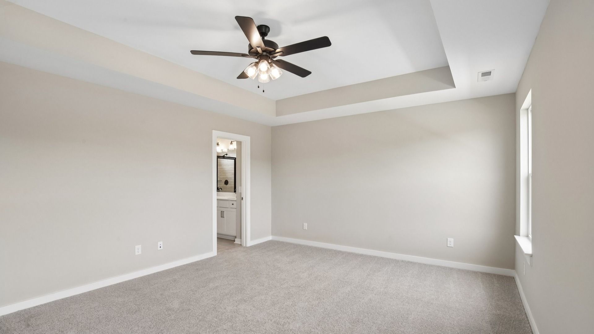 Bedroom with tray ceiling, windows, and entrance to primary bathroom