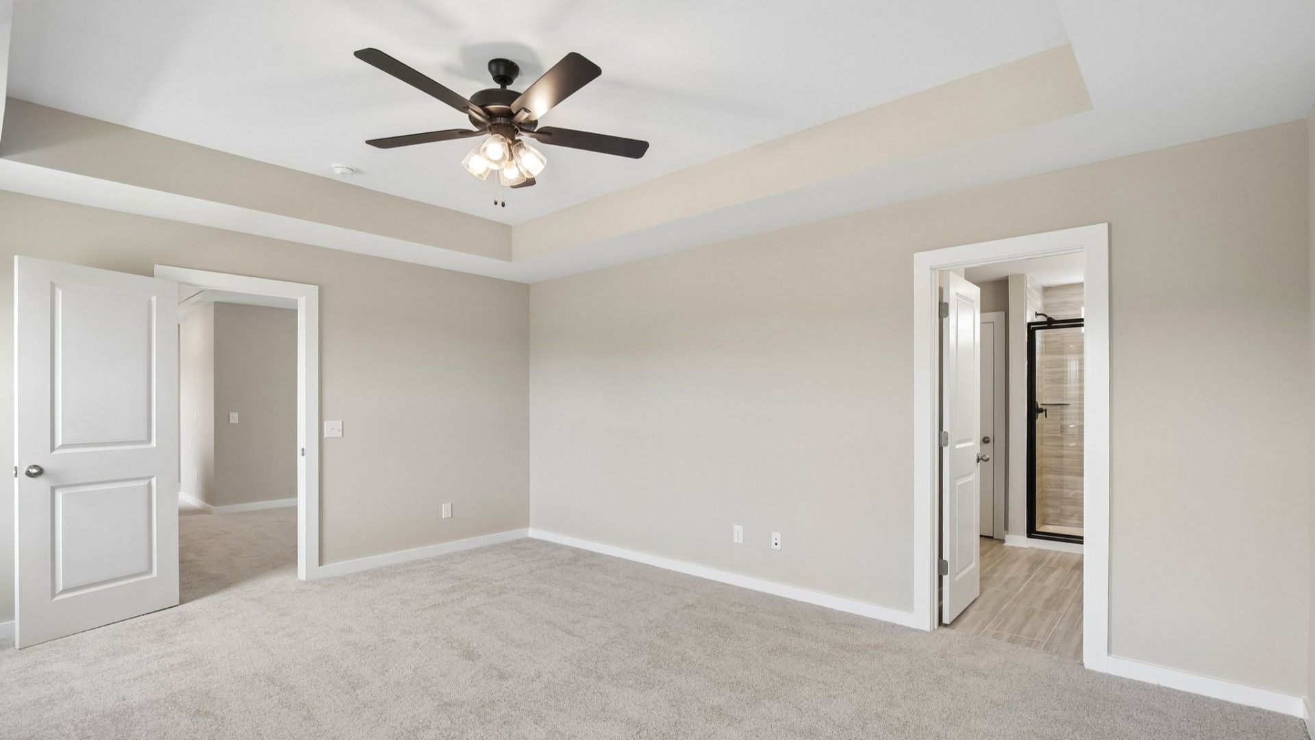 Bedroom with tray ceiling, windows, and entrance to primary bathroom