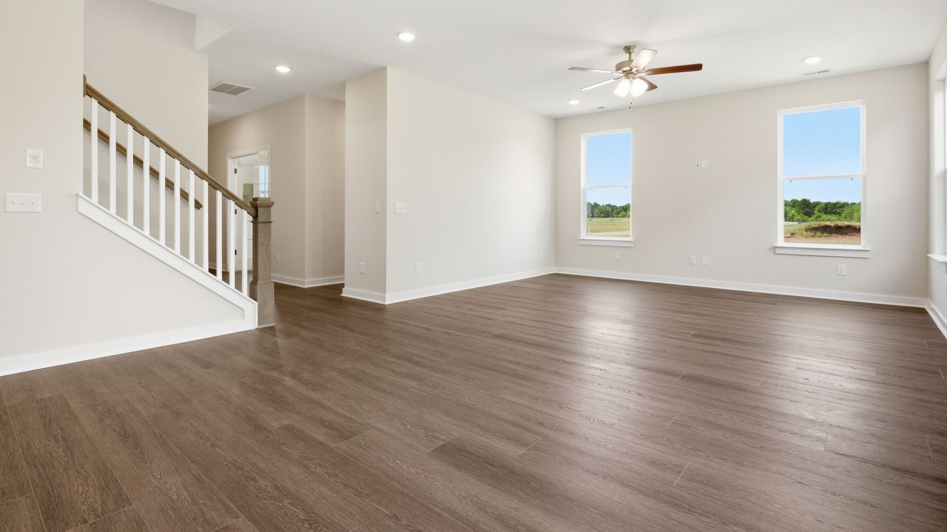 Gathering room with hard surface flooring, ceiling fan, and access to staircase