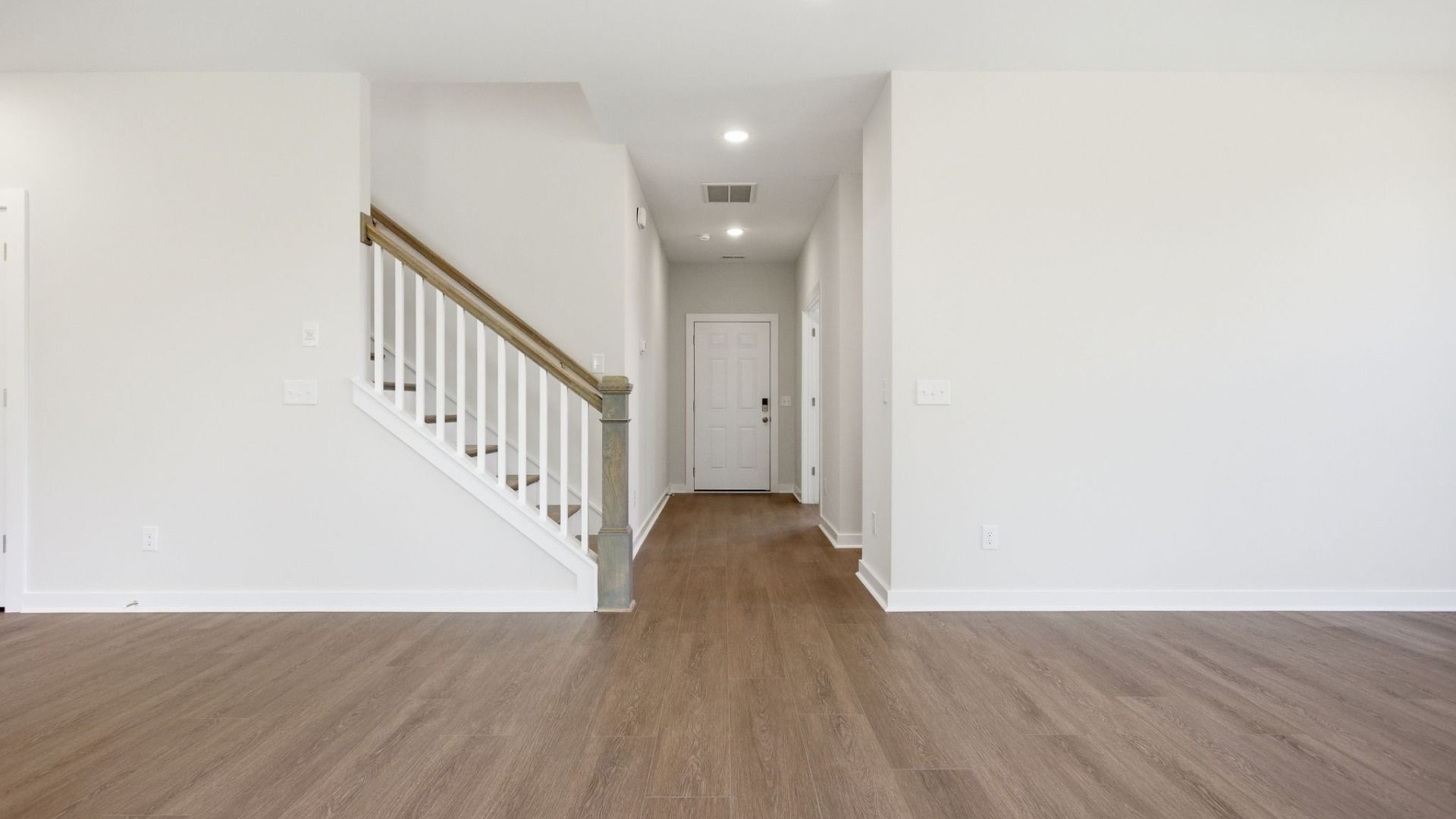 Hallway to entry door with hard surface flooring and view of staircase
