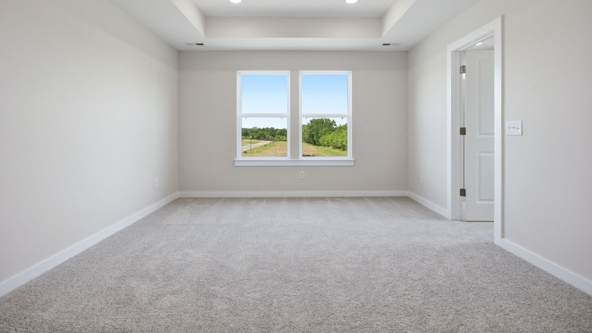 Bedroom with tray ceiling, windows, and entry to primary bathroom