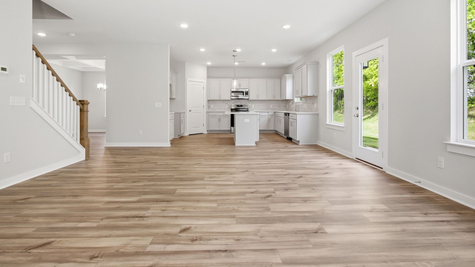 First floor with hard surface flooring, windows, nearby staircase, and view into the kitchen