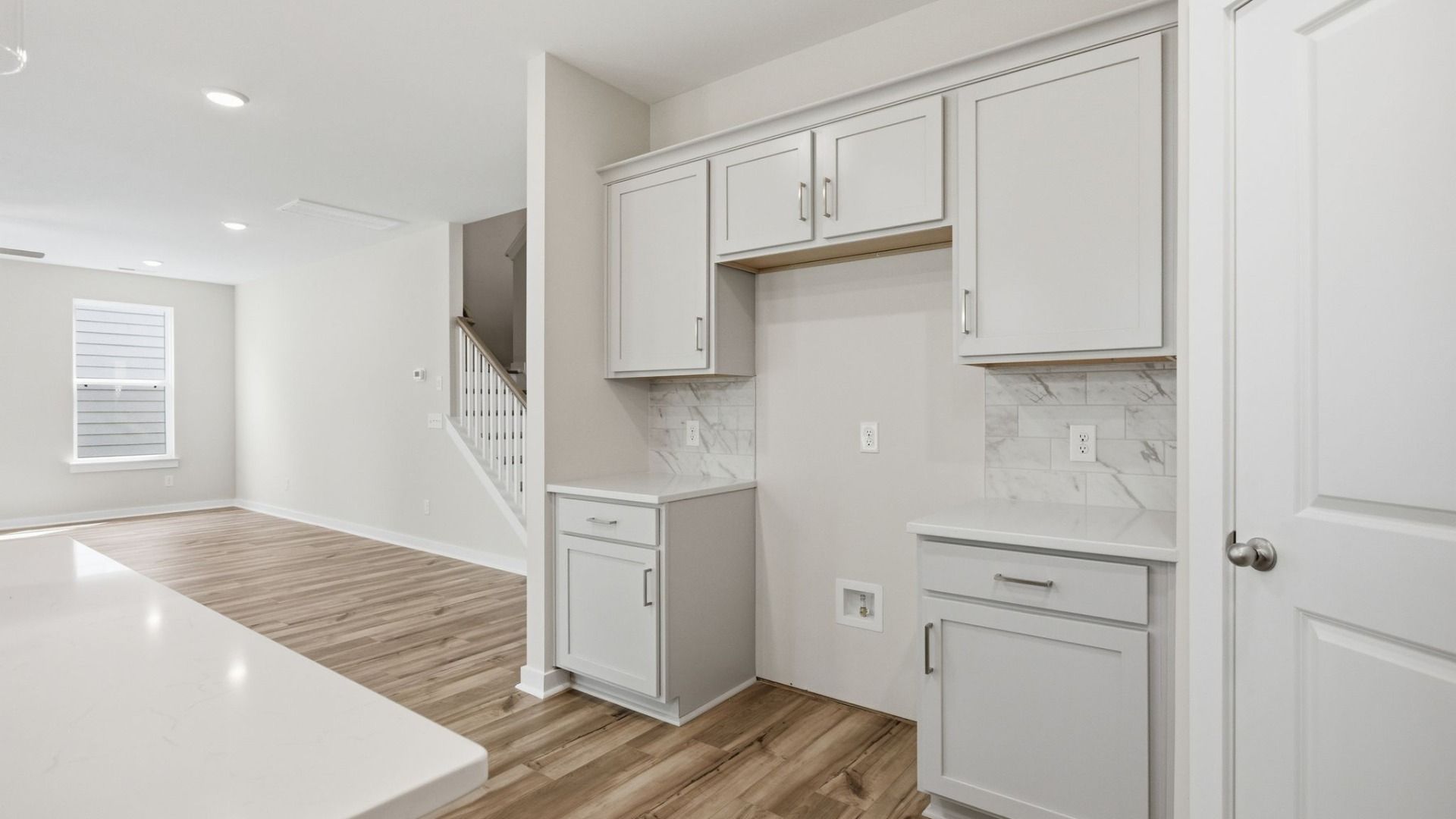 Kitchen with light cabinetry, quartz countertops, tile backsplash, and pantry with view into gathering room and staircase