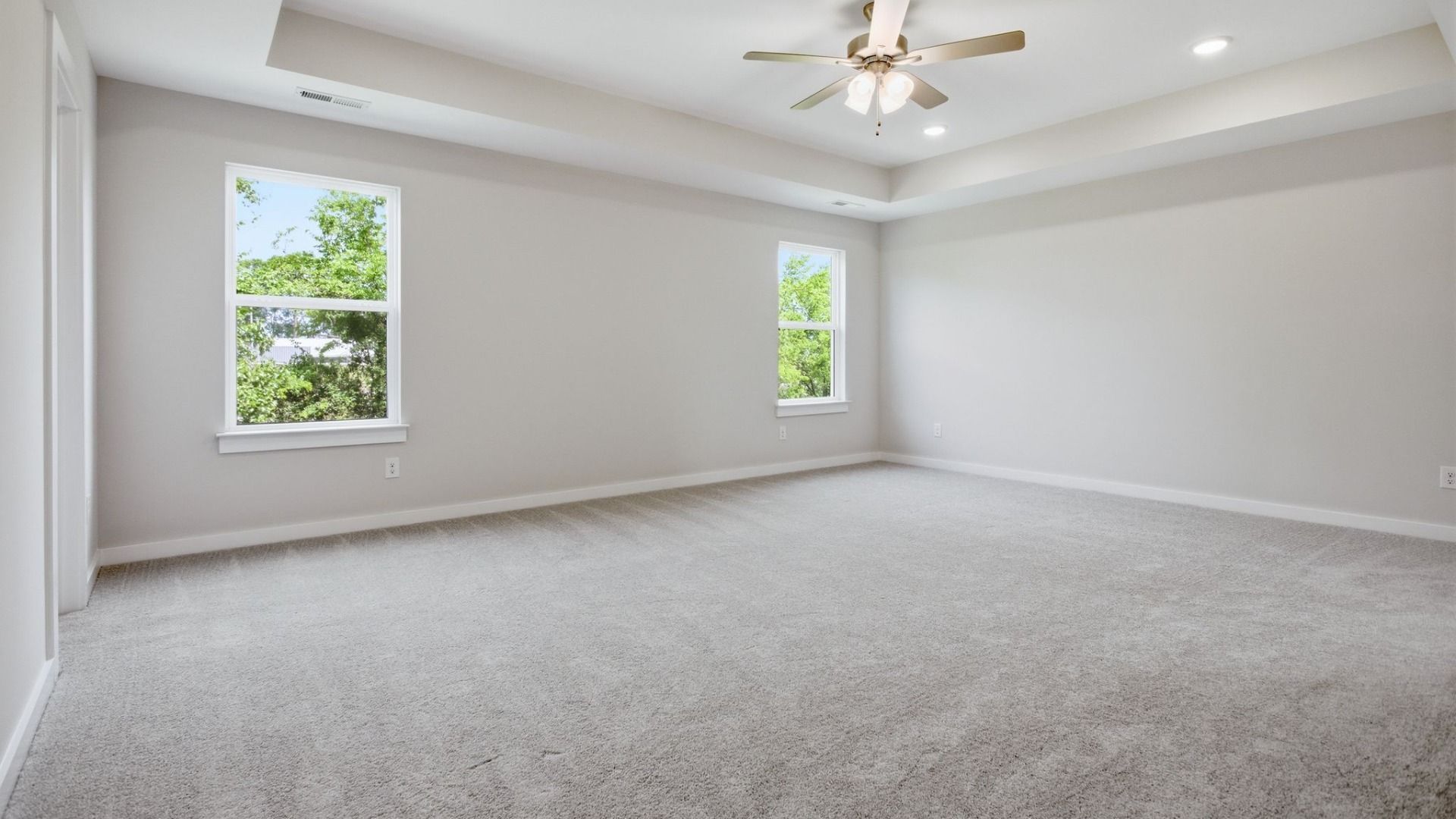Bedroom with tray ceiling, windows, and ceiling fan