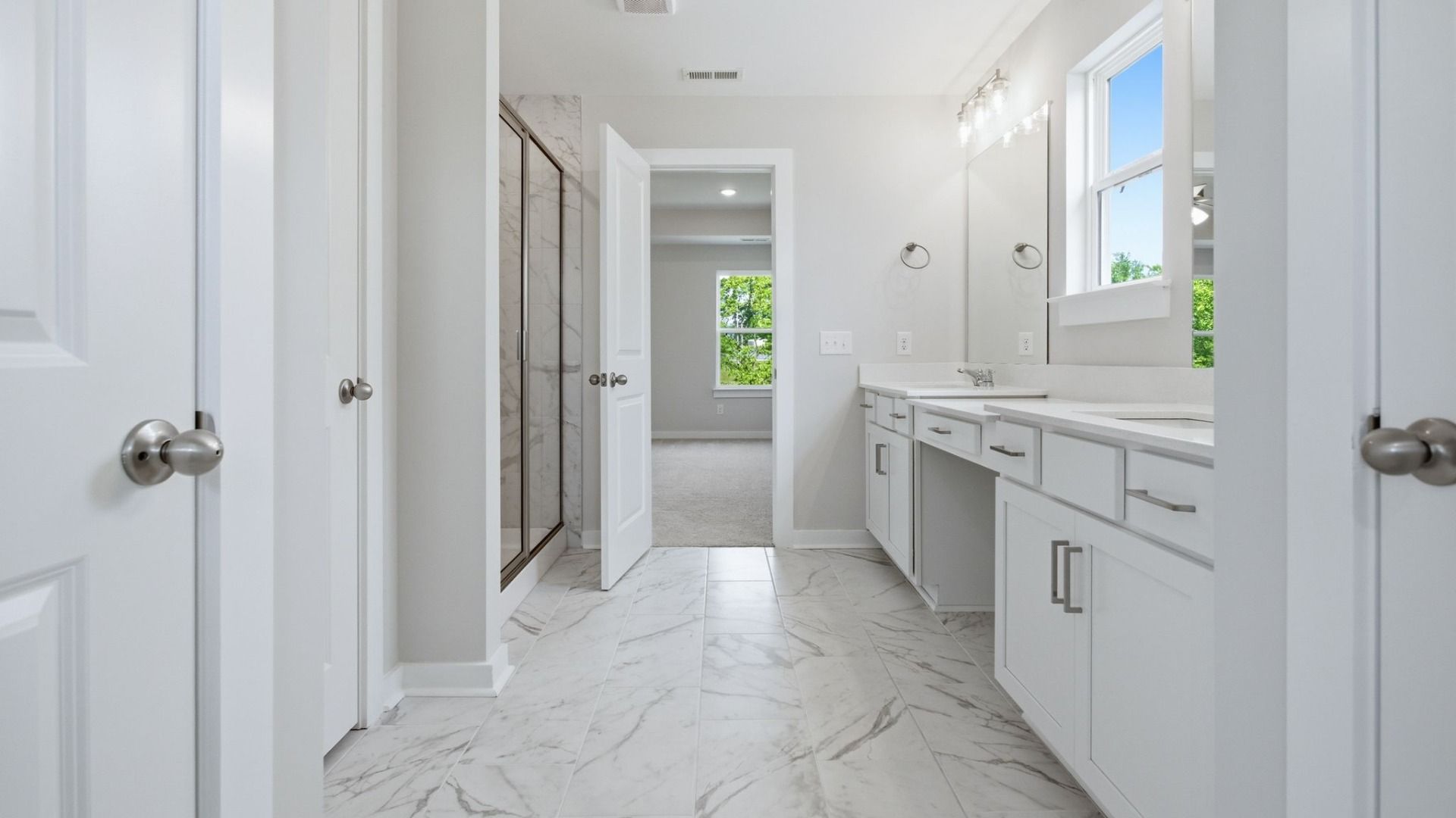 Bathroom with access to separate toilet, along with glass enclosed shower and dual vanity leading to primary suite