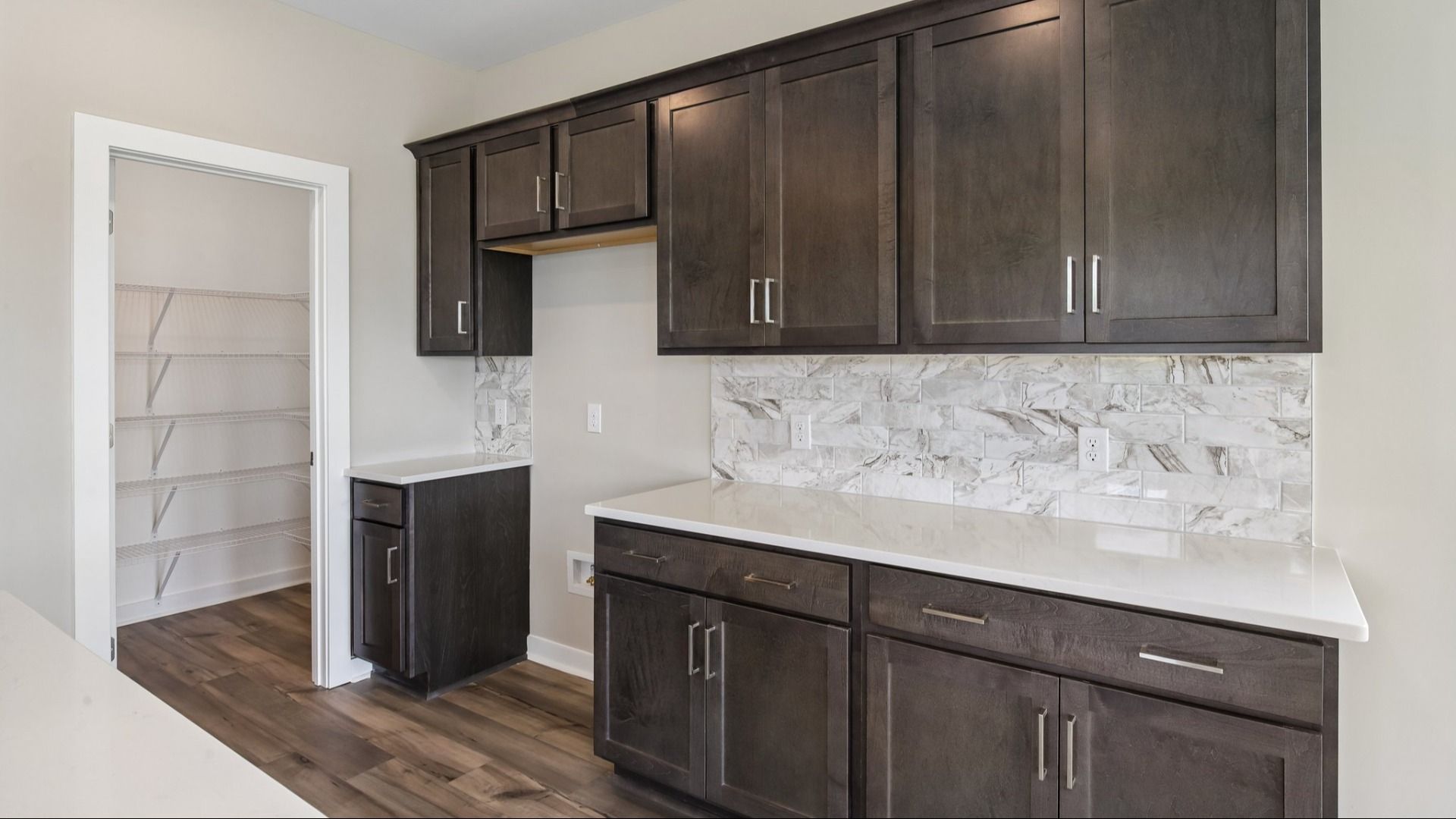Kitchen with dark cabinetry, quartz countertops, tile backsplash, and pantry