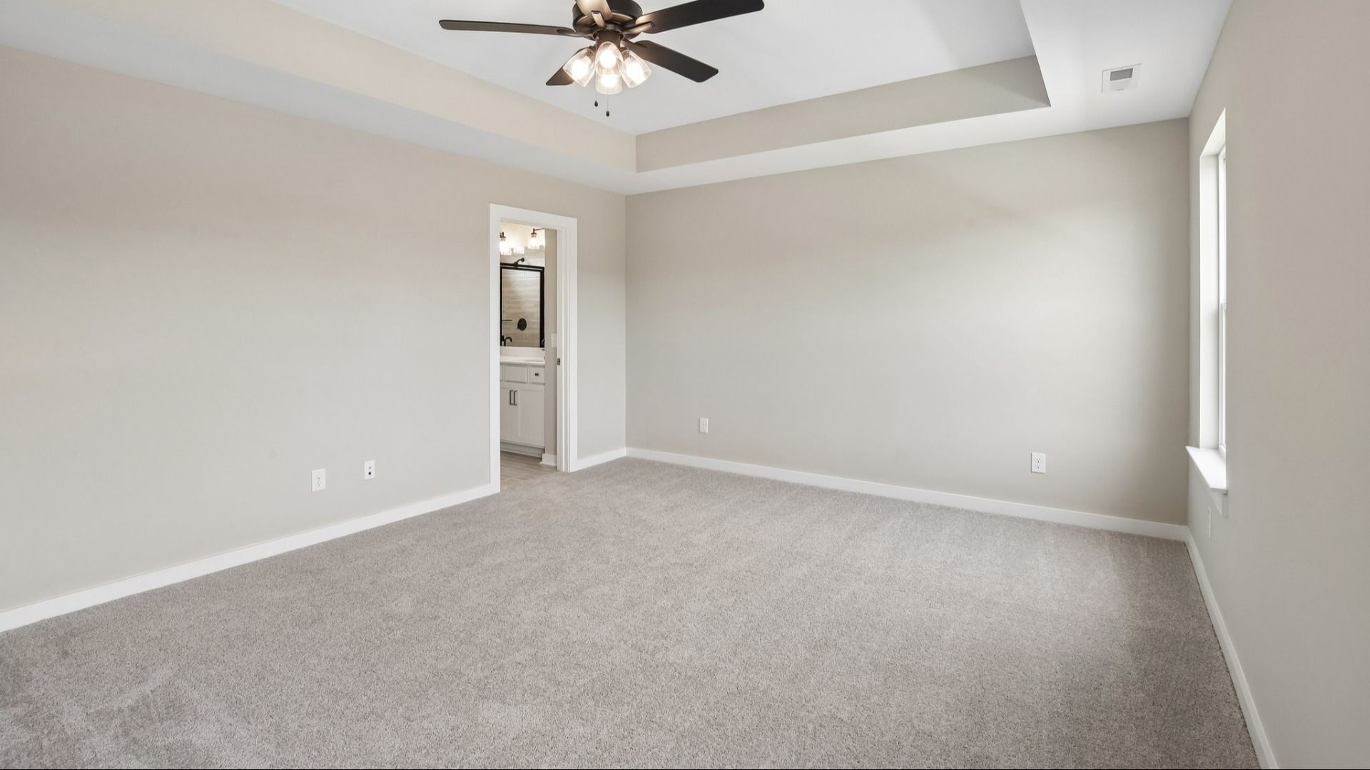 Bedroom with tray ceiling, windows, ceiling fan, and entrance to primary bathroom