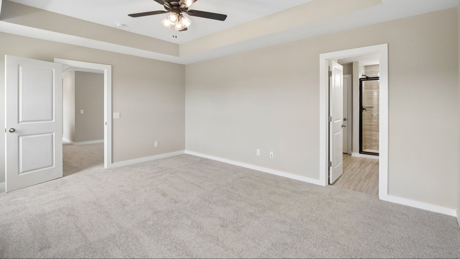 Bedroom with tray ceiling, ceiling fan, and entrance to primary bathroom