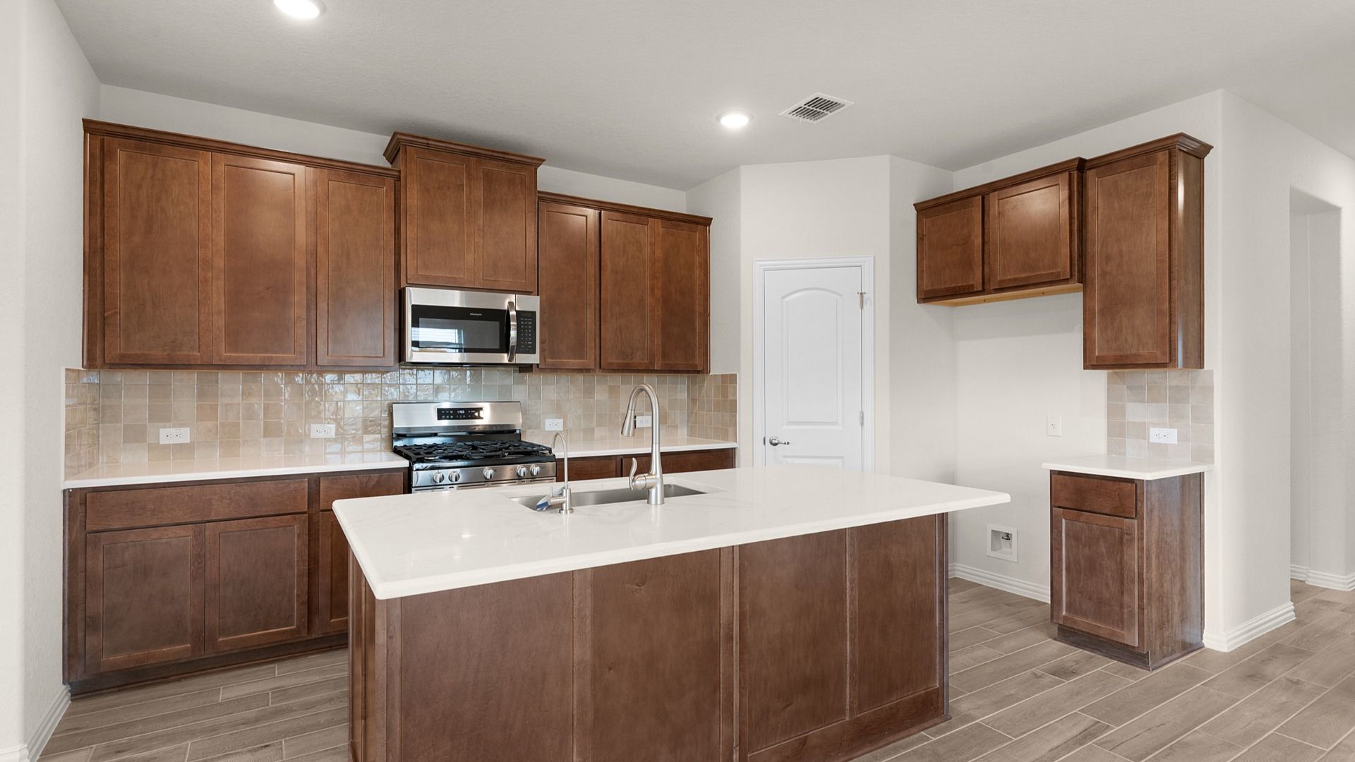 Brown 42-inch cabinetry, neutral backsplash, and center island with white countertops for a warm, modern kitchen.