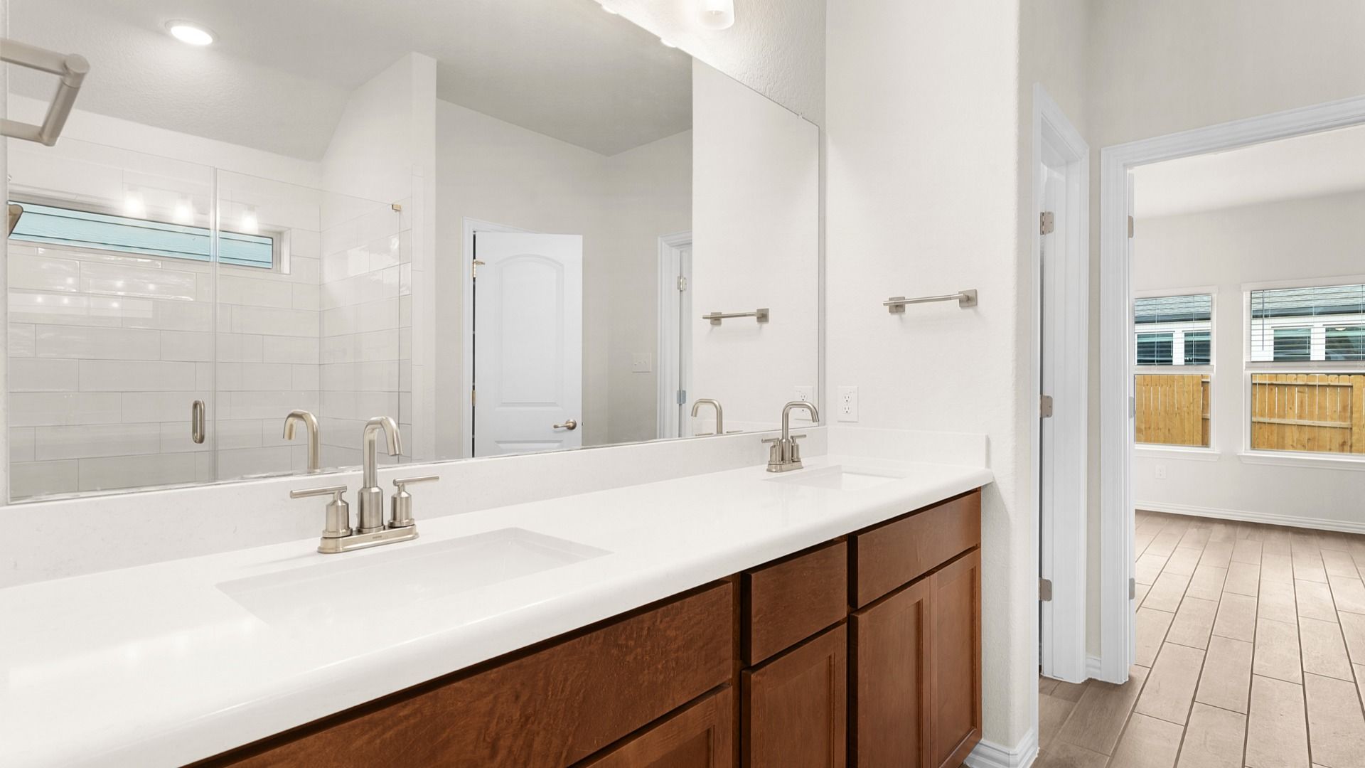 Dual vanity, frameless glass shower with white ceramic tile, and a window for bright, spa-like comfort.