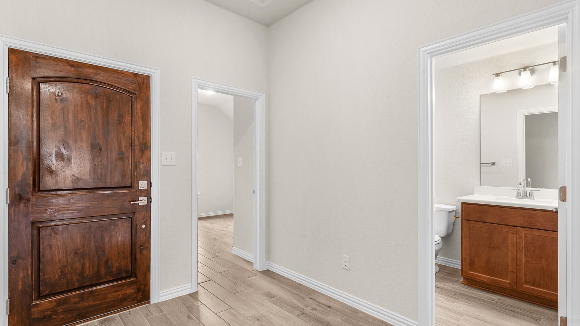 Solid wood front door opens to convenient entryway with nearby bathrooms, blending style, function, and easy access.