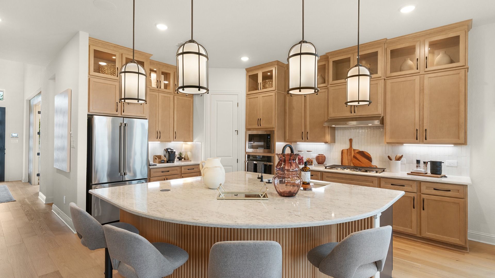 Modern kitchen with ceiling-height cabinets, built-in appliances, statement lighting, and a large center island.
