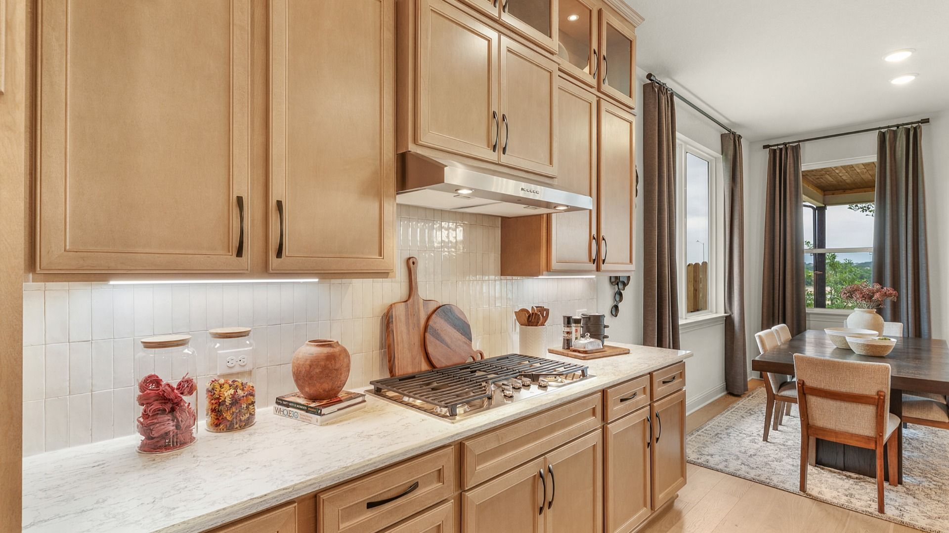 Kitchen features a stainless vent hood, cabinet accent lighting, and a sleek gas cooktop.