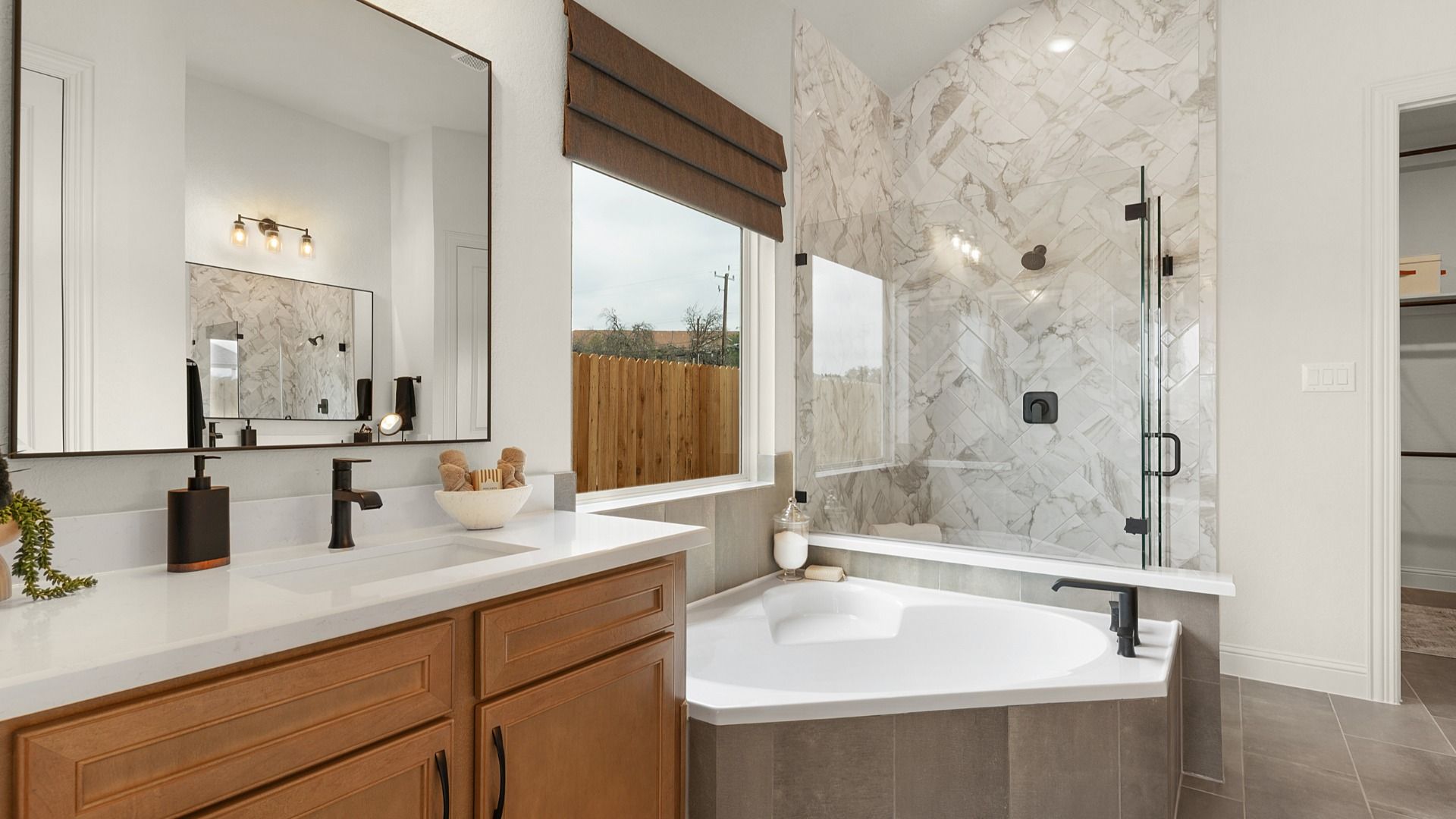 Owner’s bath features a modern design with a separate garden tub, frameless glass shower, and ceramic tile.