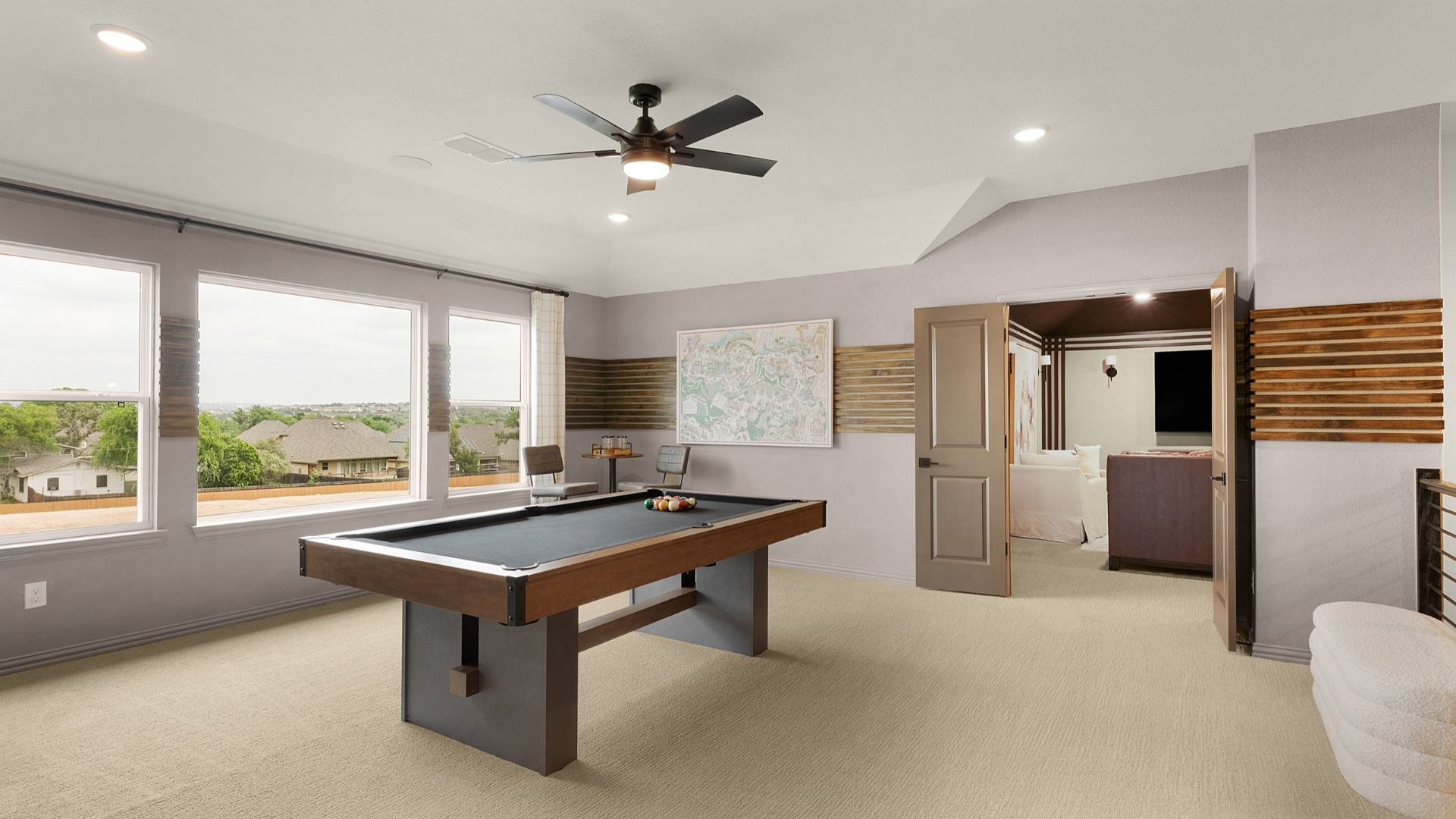 Second-floor game room with large windows and a ceiling fan, connected to a dedicated media room for entertainment.