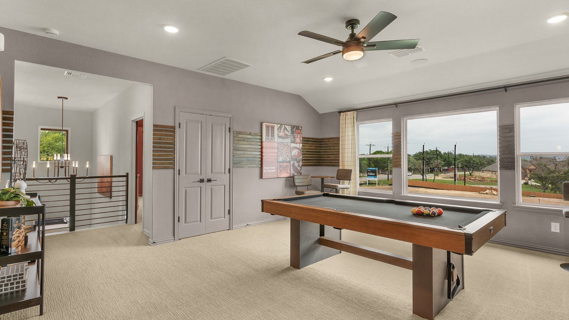 Second-floor game room with large windows and a ceiling fan, connected to a dedicated media room for entertainment.