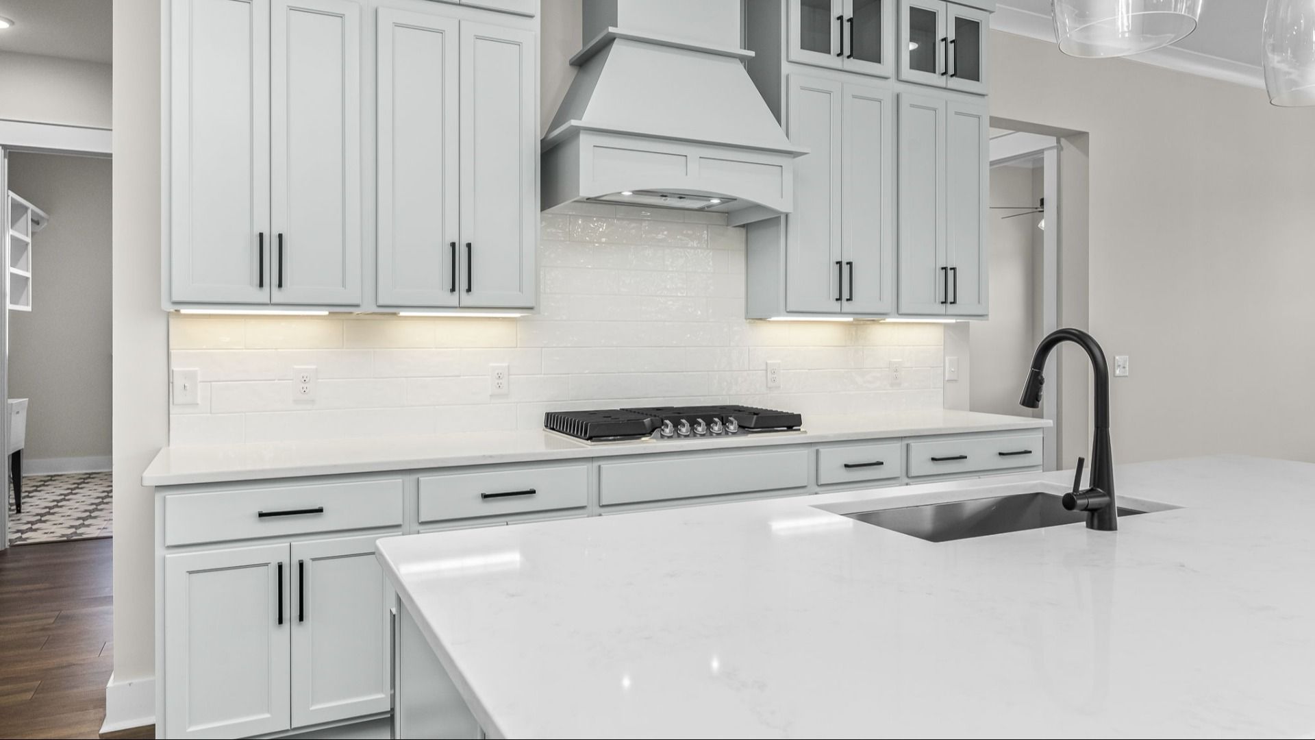 Up-close image of kitchen with light cabinetry, tile backsplash, and quartz countertops