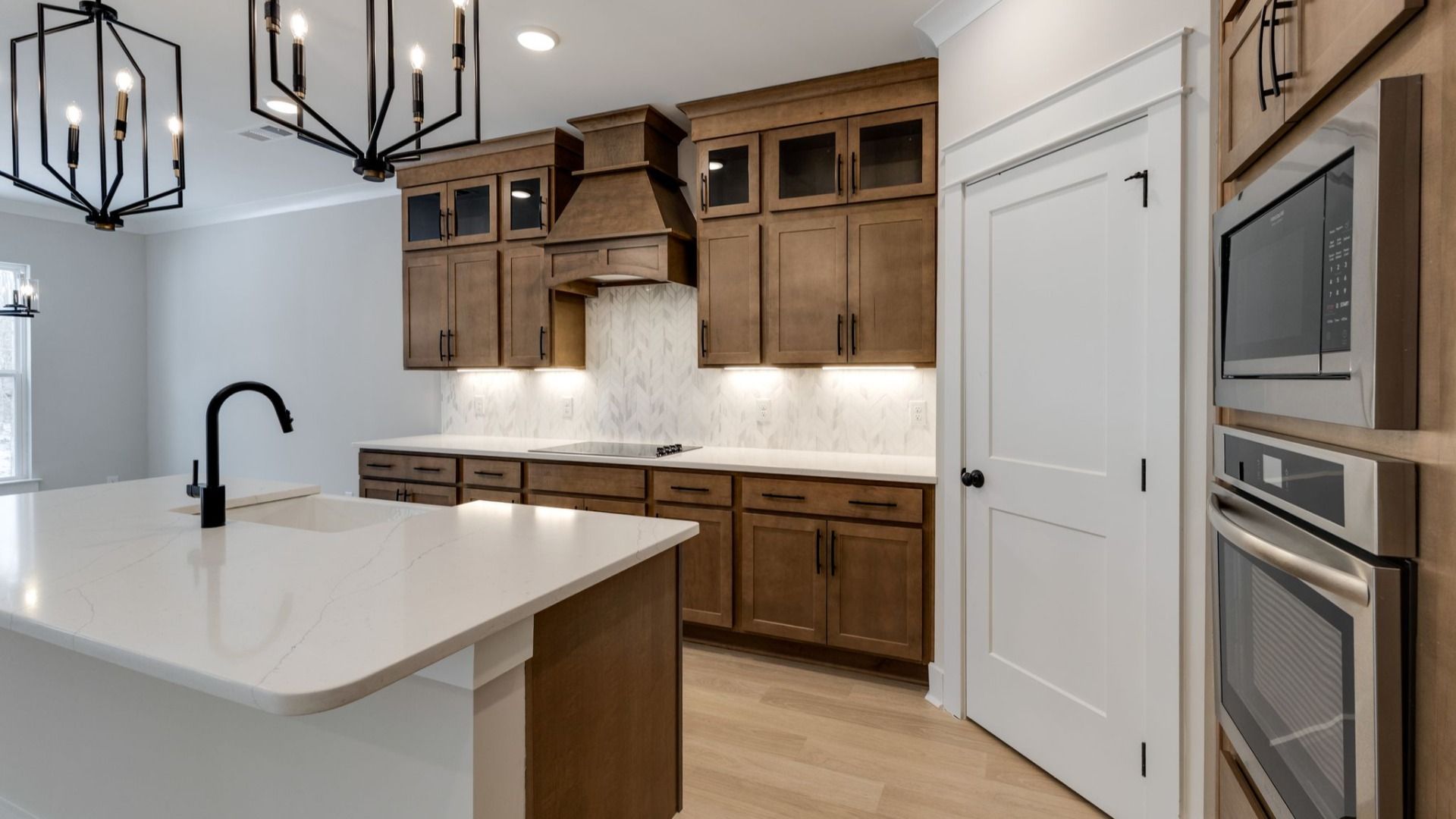 Luxurious kitchen with tasteful dark cabinetry, pendent lighting, tile backsplash, and pantry