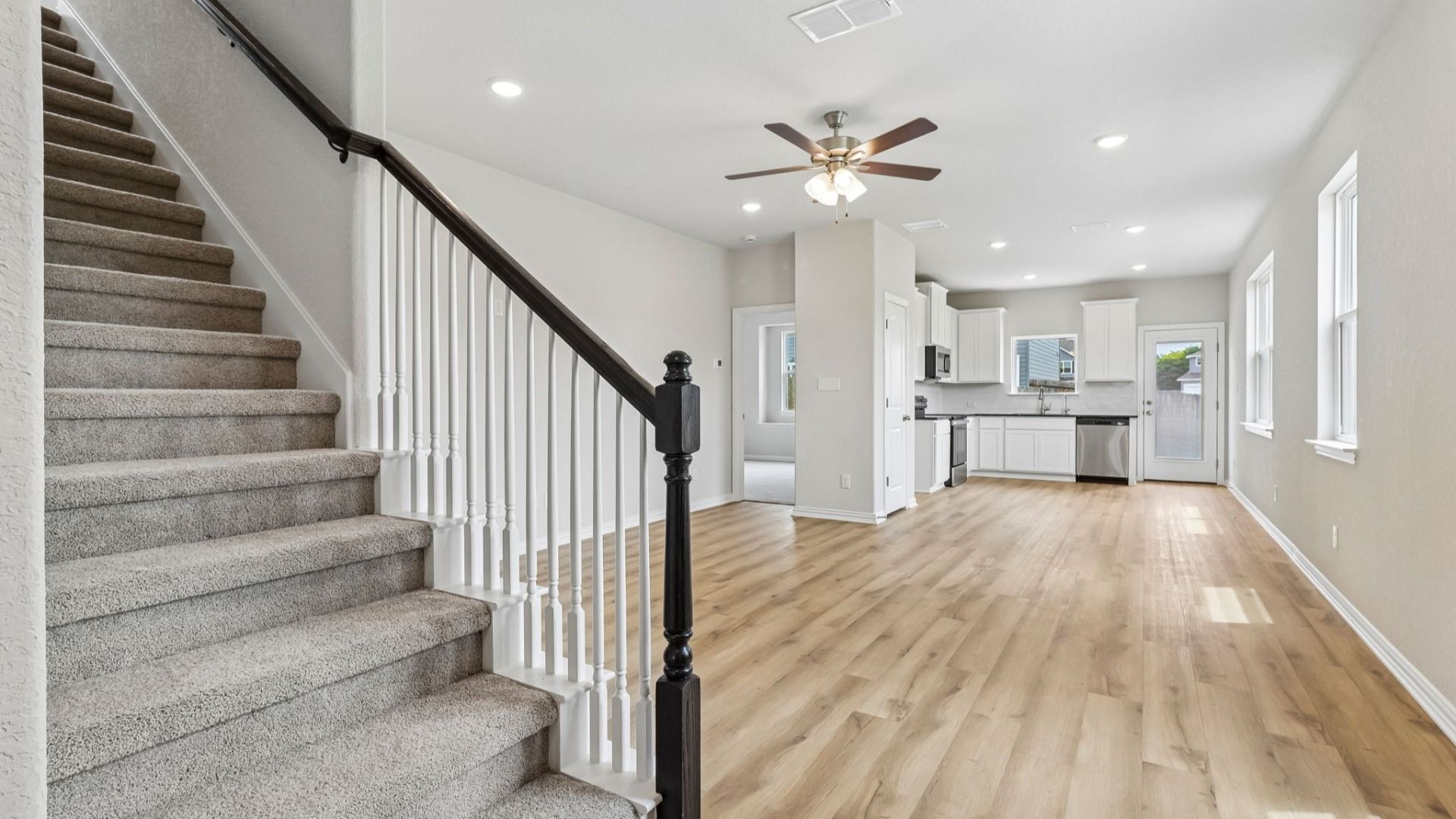 Stairs with stained wooden railing, Great Room includes ceiling fan and opens to kitchen
