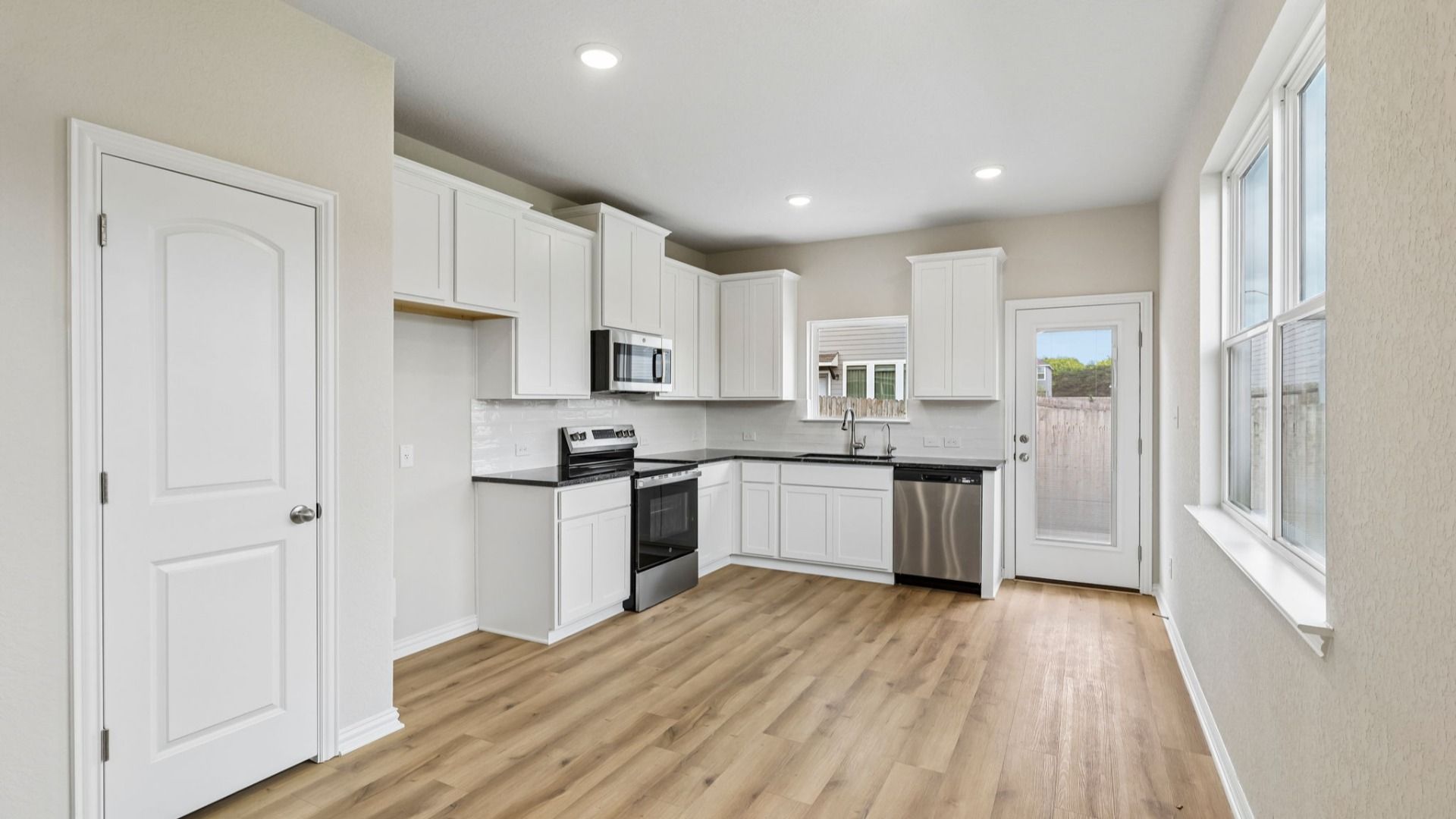 Kitchen is bright with 42 inch white cabinetry, sleek contrasting black countertops, and stainless steel appliances