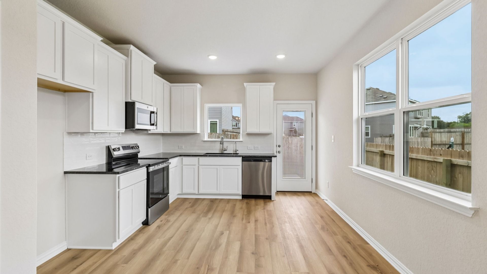 Kitchen is bright with 42 inch white cabinetry, sleek contrasting black countertops, and stainless steel appliances