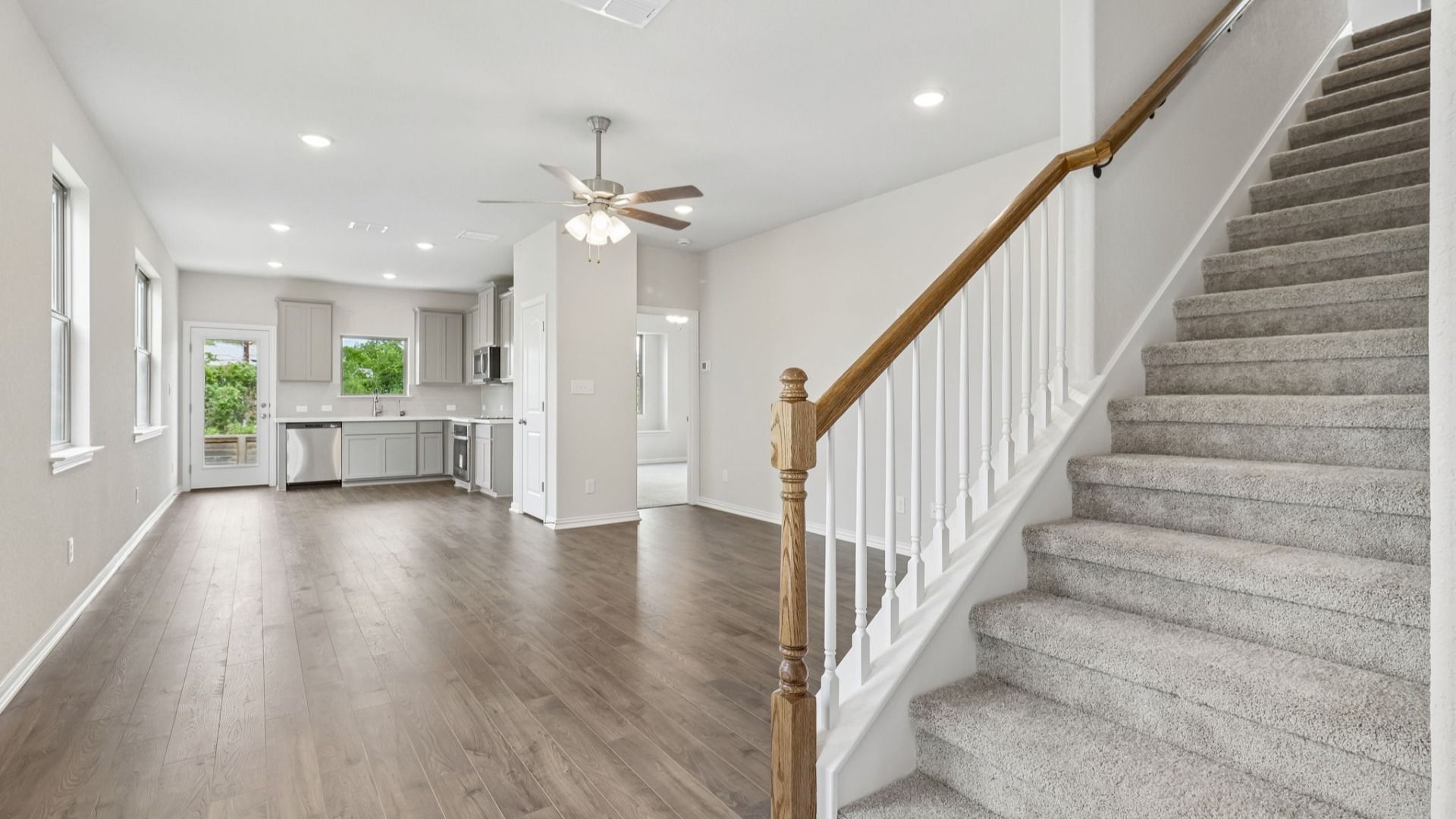 Stairs with stained wooden railing, Great Room includes ceiling fan and opens to kitchen