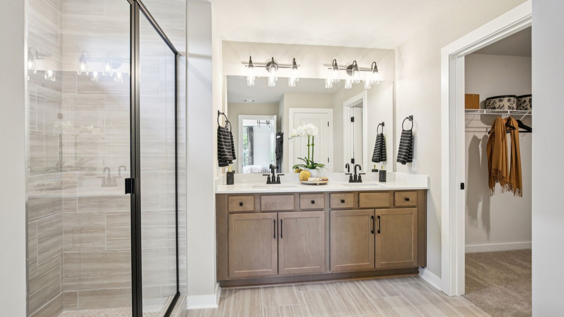 Spacious bathroom with tiled shower with glass enclosure, dual vanity area, and walk-in closet