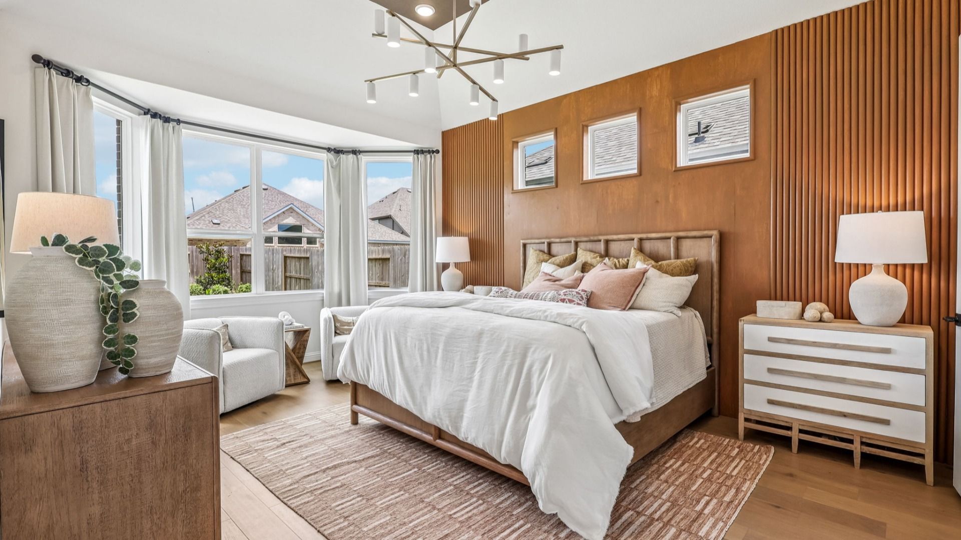 Luxurious bedroom with wood paneling, designer chandelier, and expansive windows in Brookewater community.