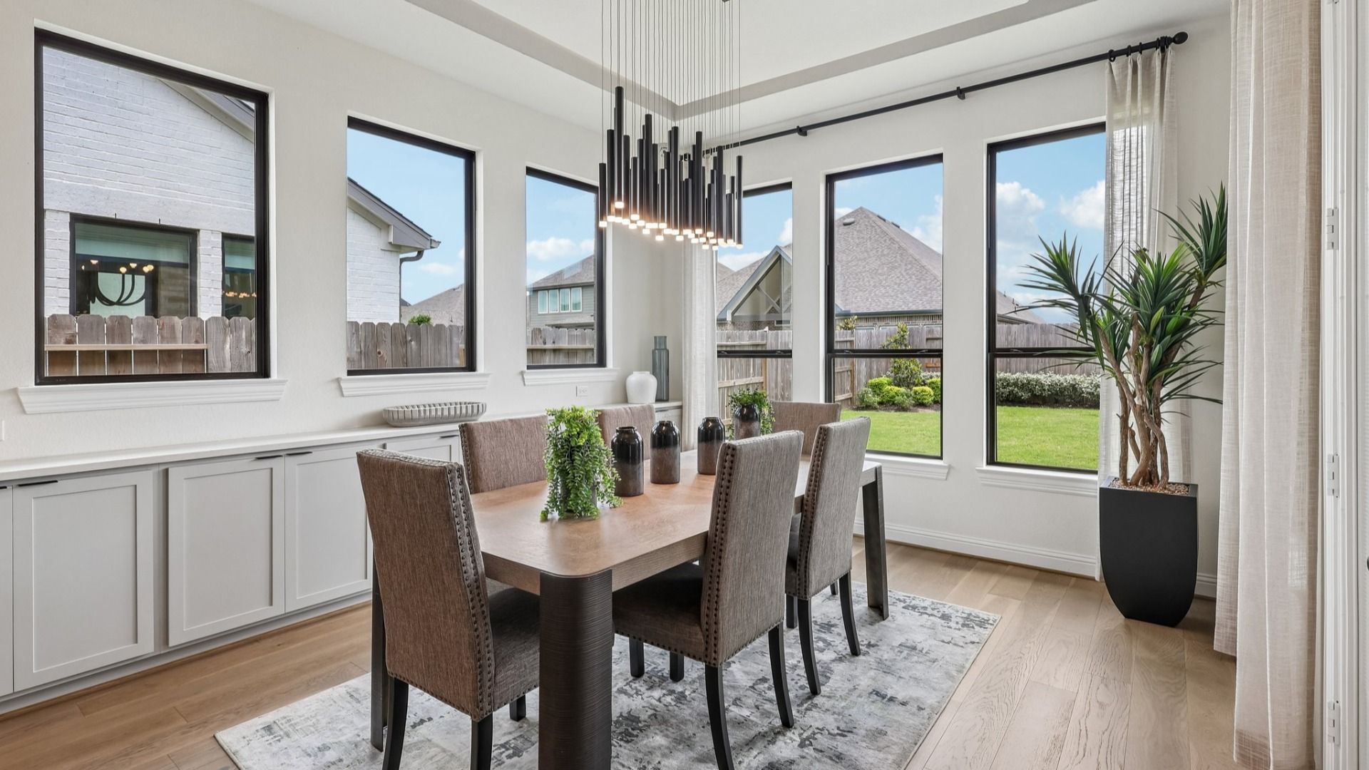 Sunlit dining space with chic chandelier and expansive windows in Brookewater. Luxurious hardwood floors enhance elegance.
