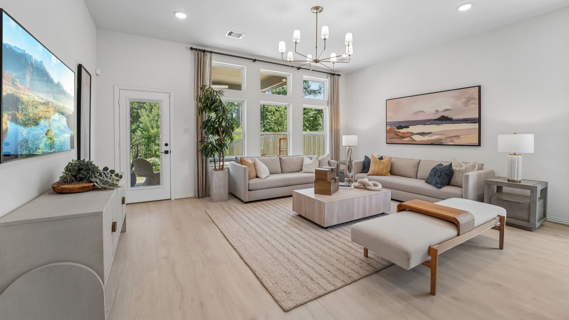 Luxurious living room boasts modern chandelier, expansive windows, and refined décor in The Woodlands Hills.