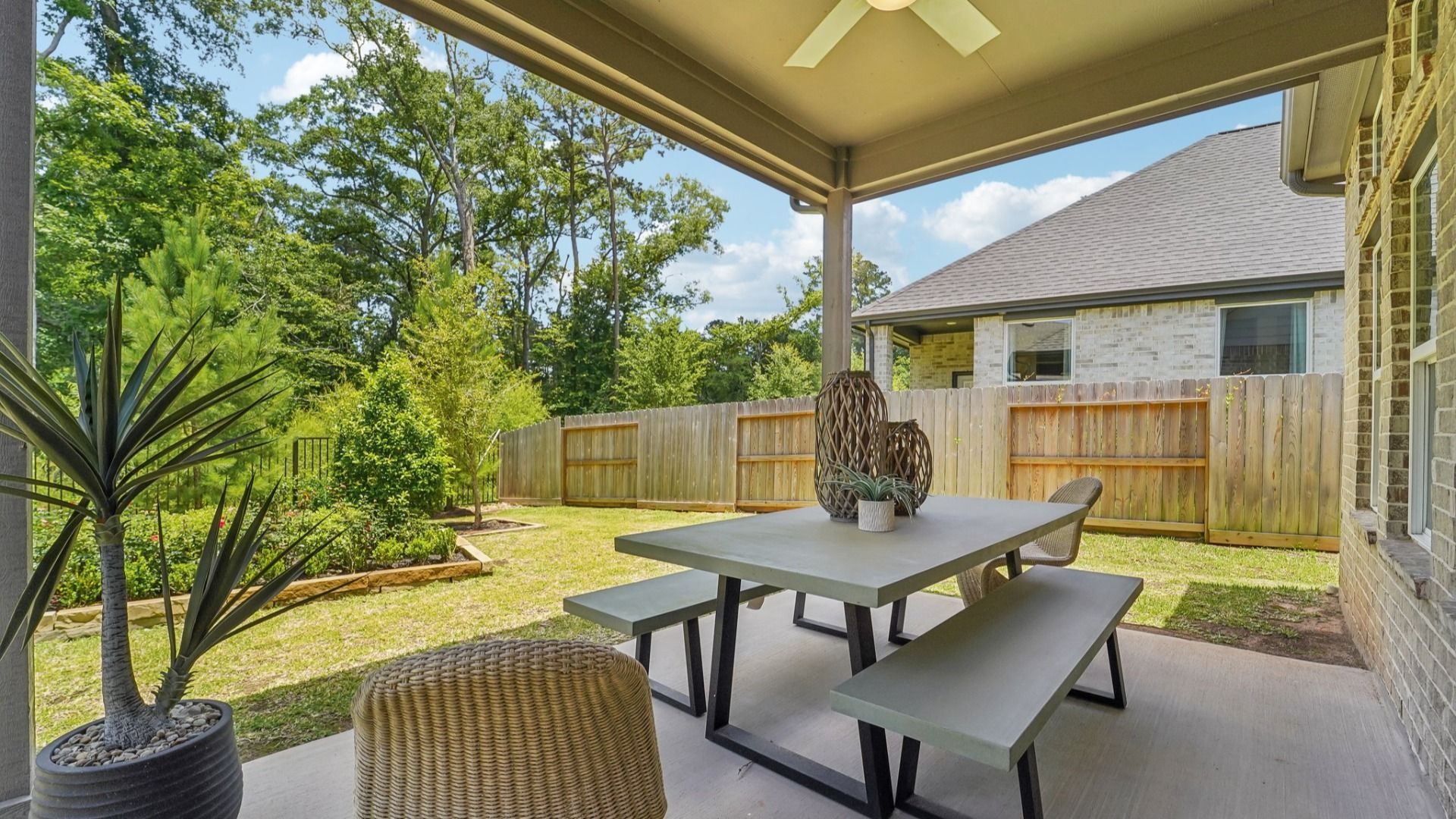 Elegant brick façade with a covered patio, ceiling fan, and lush garden. The Woodlands Hills community.