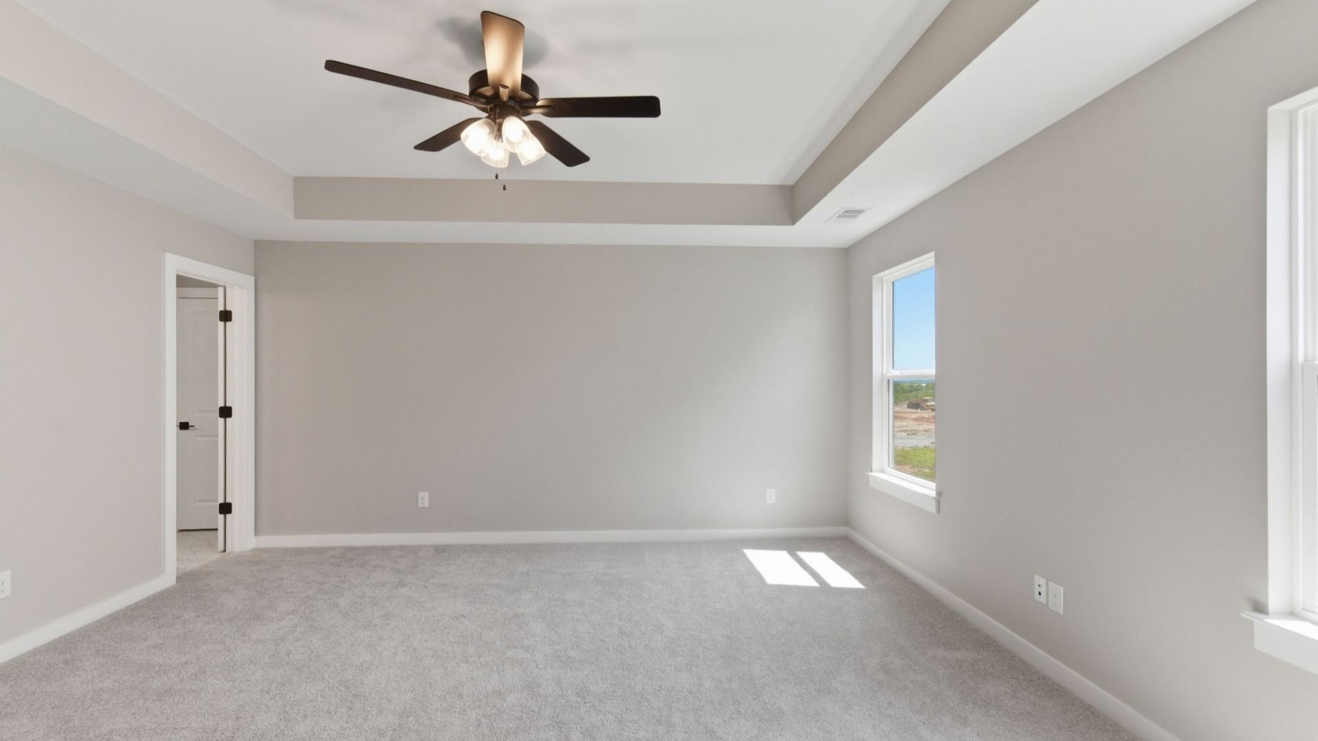 Primary suite with tray ceiling, ceiling fan, and carpet