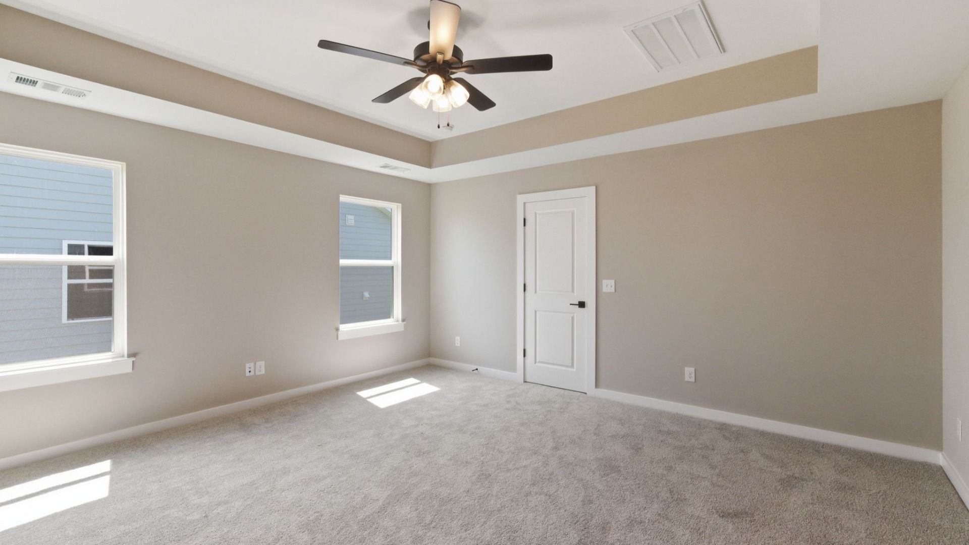Primary suite with tray ceiling, ceiling fan, and carpet
