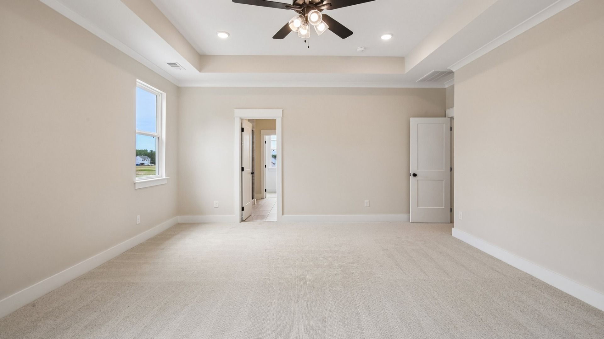 Primary suite with tray ceiling, ceiling fan, and carpet