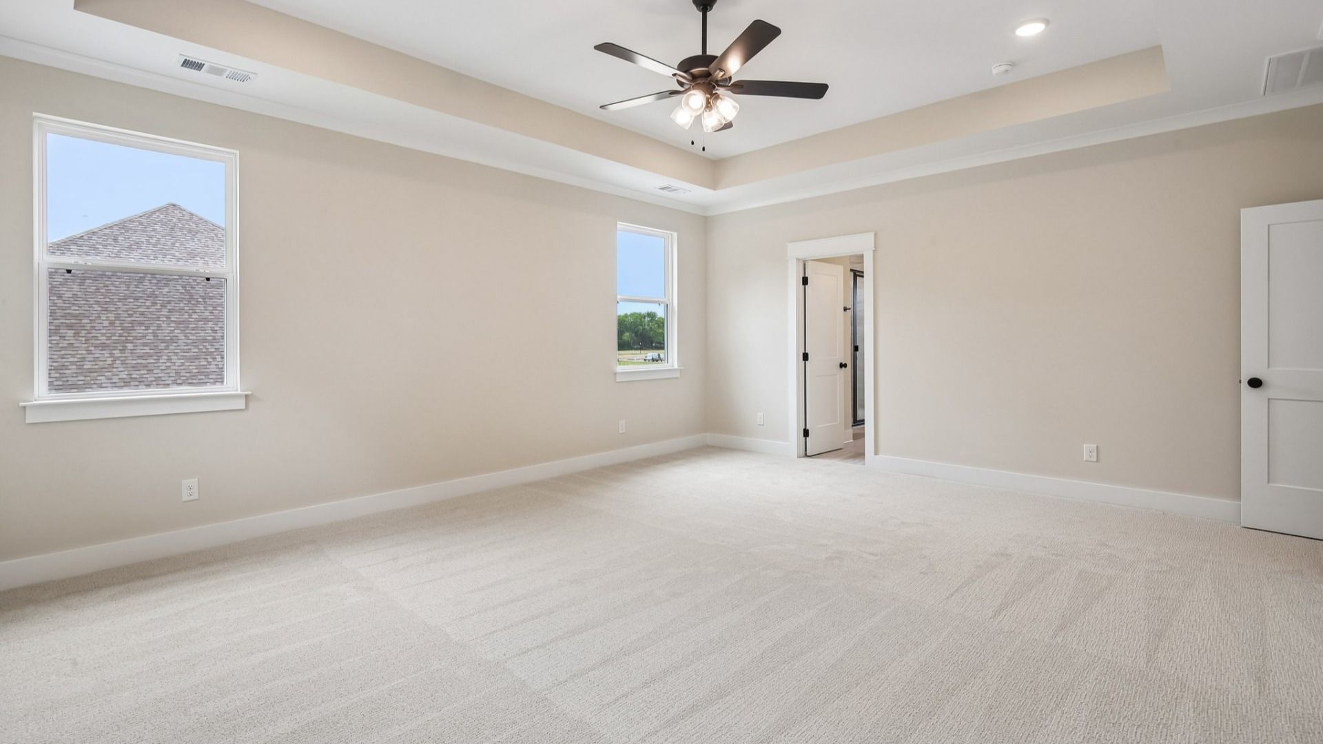 Primary suite with tray ceiling, ceiling fan, and carpet