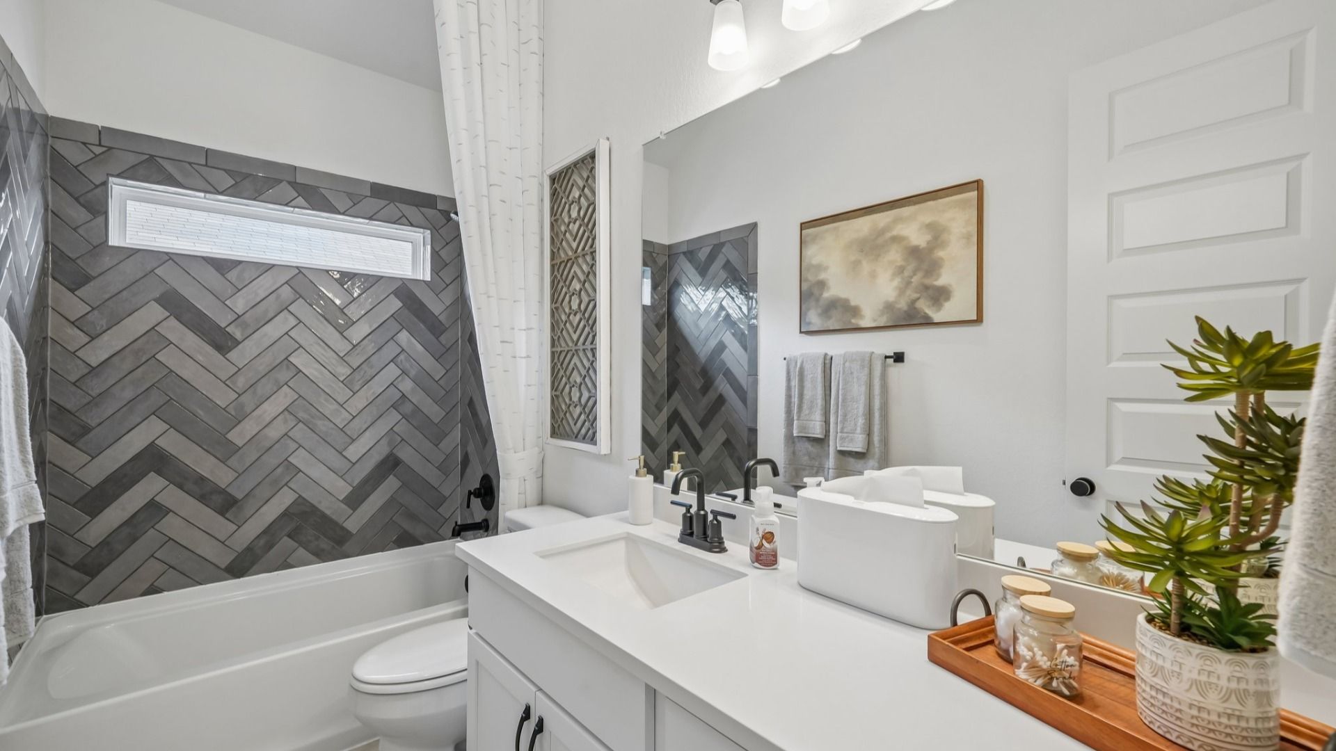 Secondary bedroom featuring gray tile tub/shower combo, natural light window, and single vanity with spacious counter