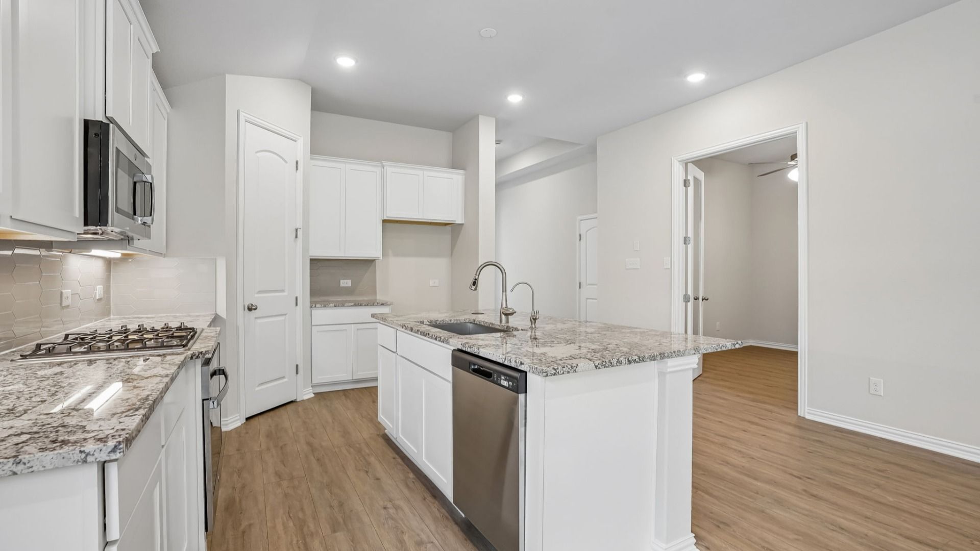 Spacious island kitchen with white cabinetry, gas cooktop, and corner pantry.