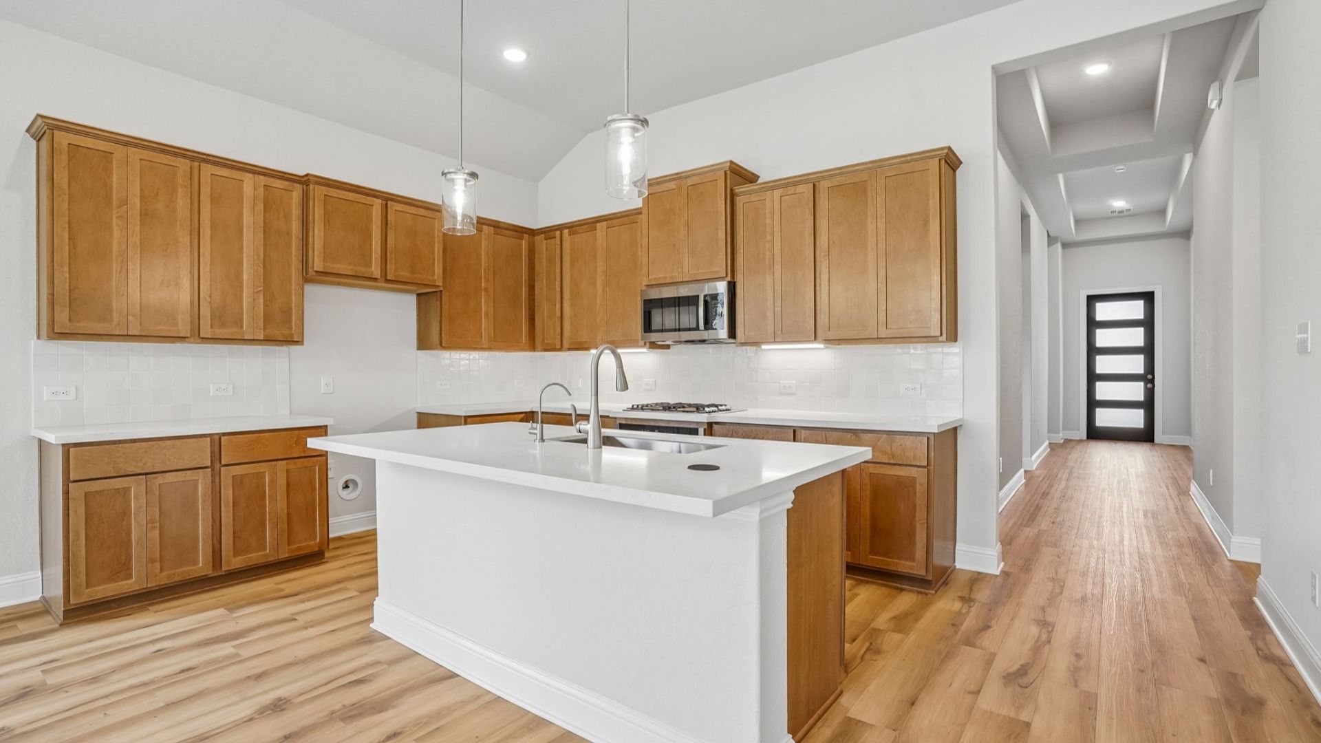The spacious kitchen island features an undermount sink, pop-up power outlet, and glass pendant lighting.