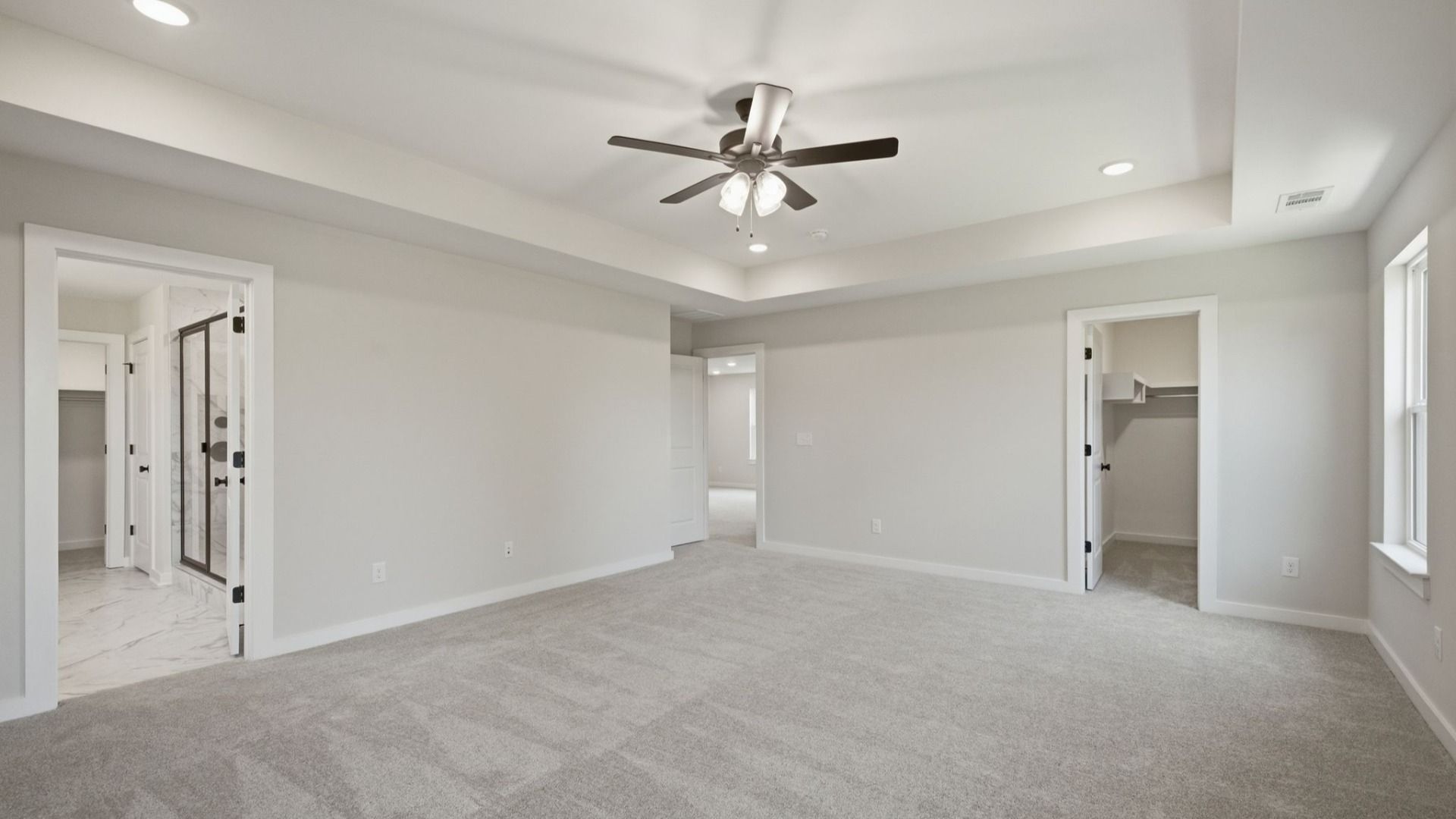 Primary suite with tray ceiling, ceiling fan, carpet, and windows