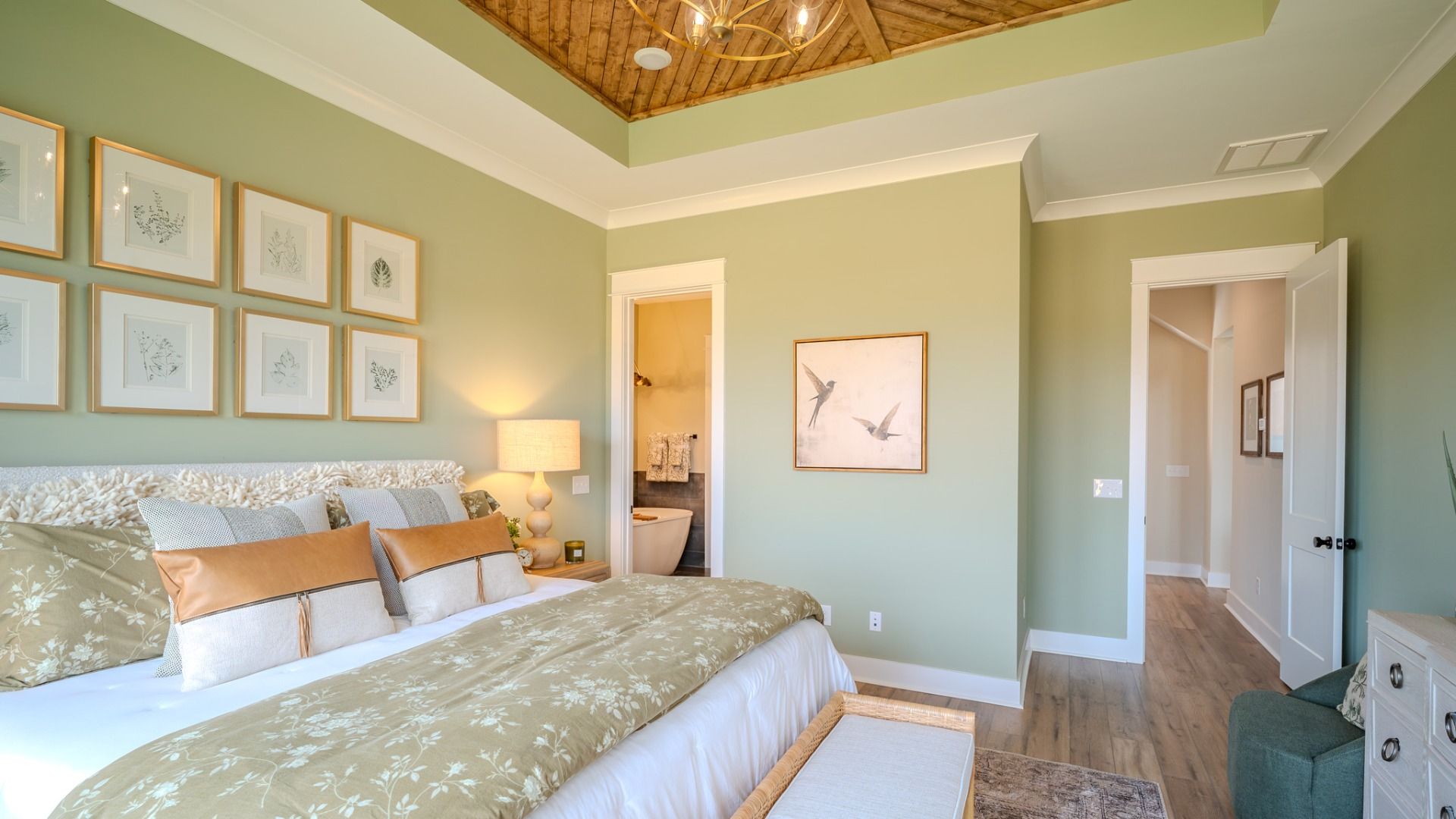 Spacious primary suite with tray ceiling, hard surface flooring, and access to primary bathroom