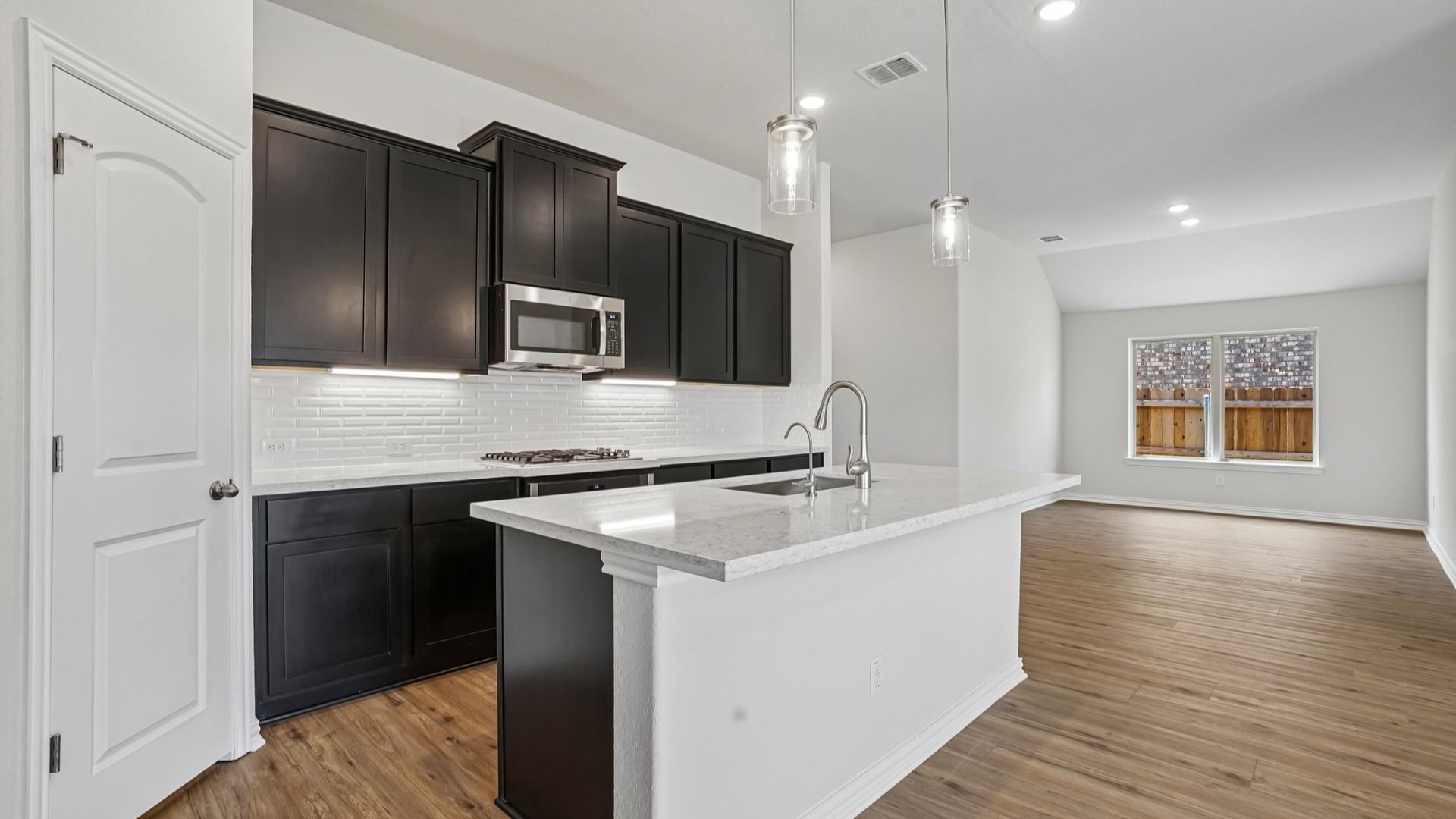 Espresso cabinets, sleek countertops, pendant lighting, center island, and gas cooking create a stylish kitchen.