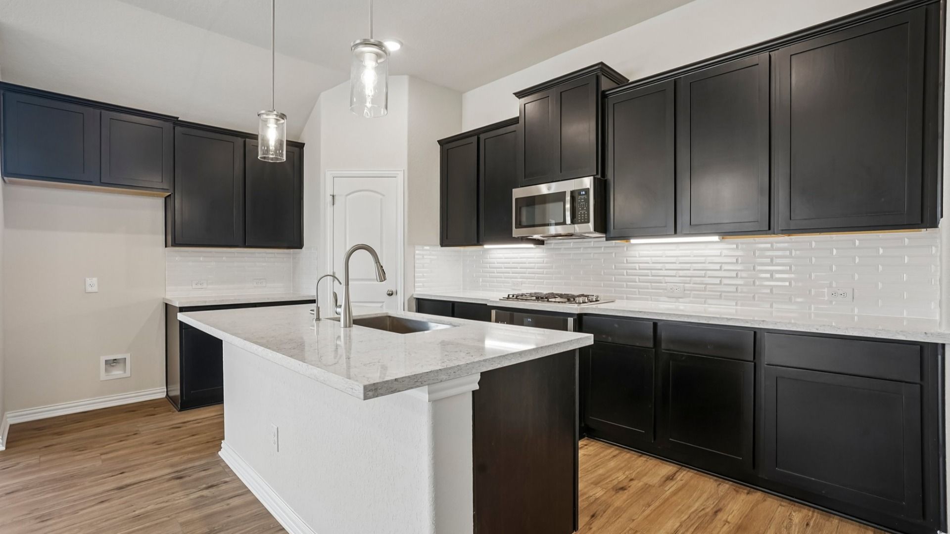 Espresso cabinets, sleek countertops, pendant lighting, center island, and gas cooking create a stylish kitchen.